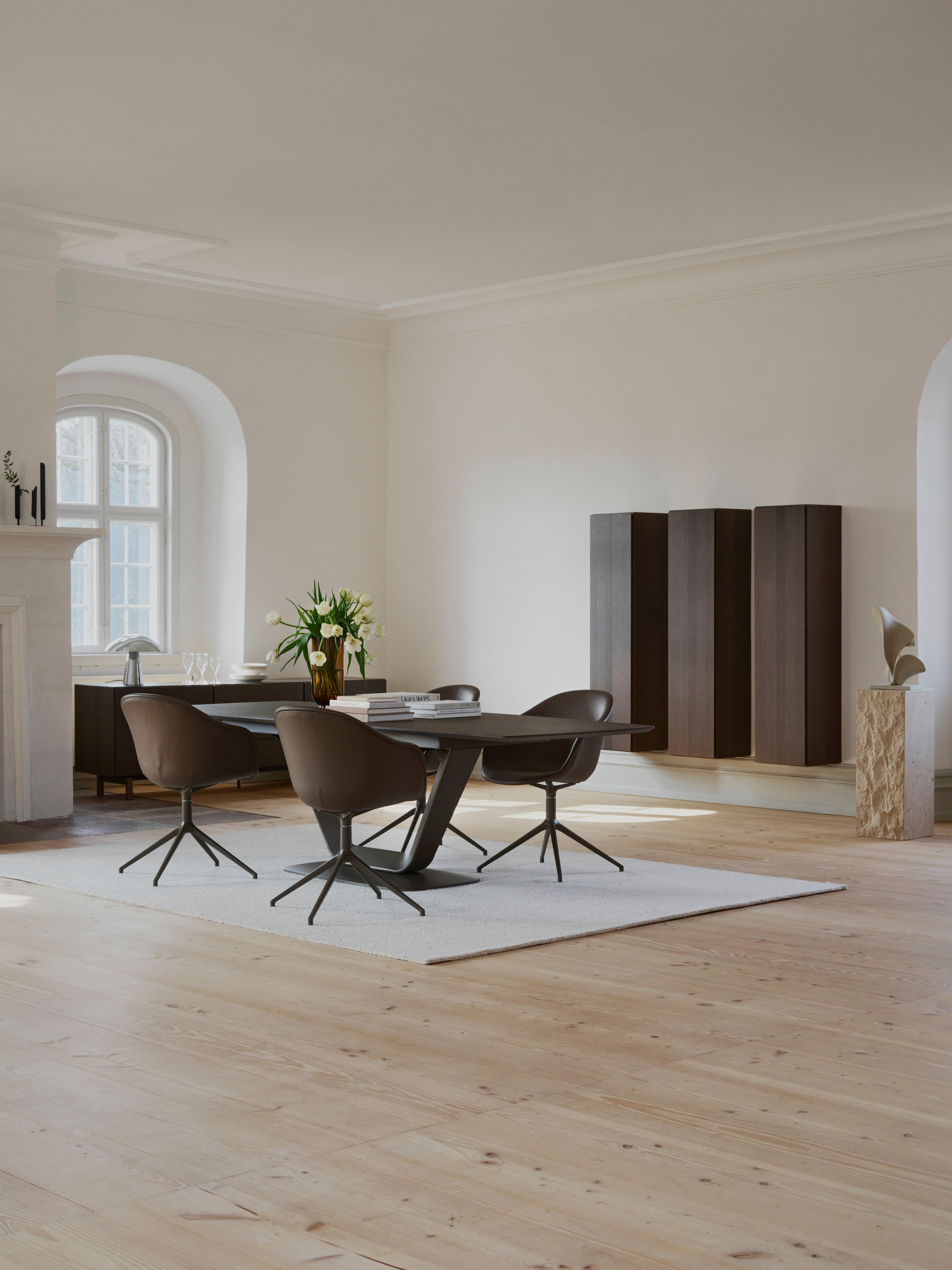 Modern dining table with four swivel chairs, books and a vase of flowers.