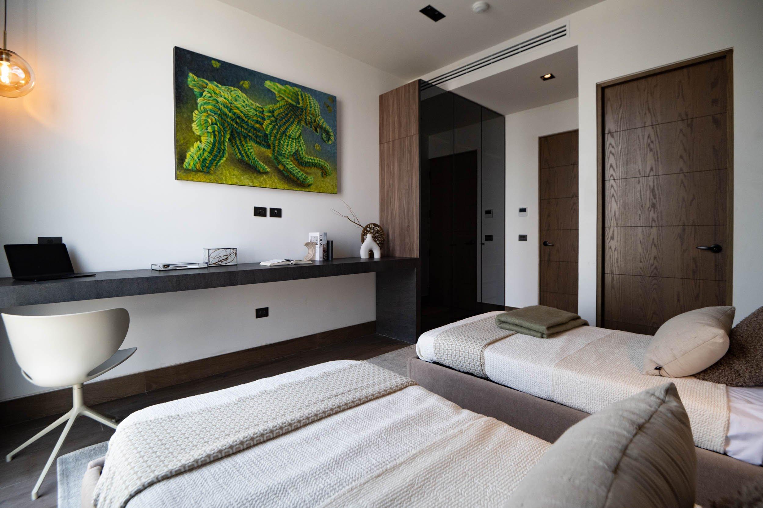 Chambre avec deux lits simples, bureau mural et tableau d’un éléphant vert.
