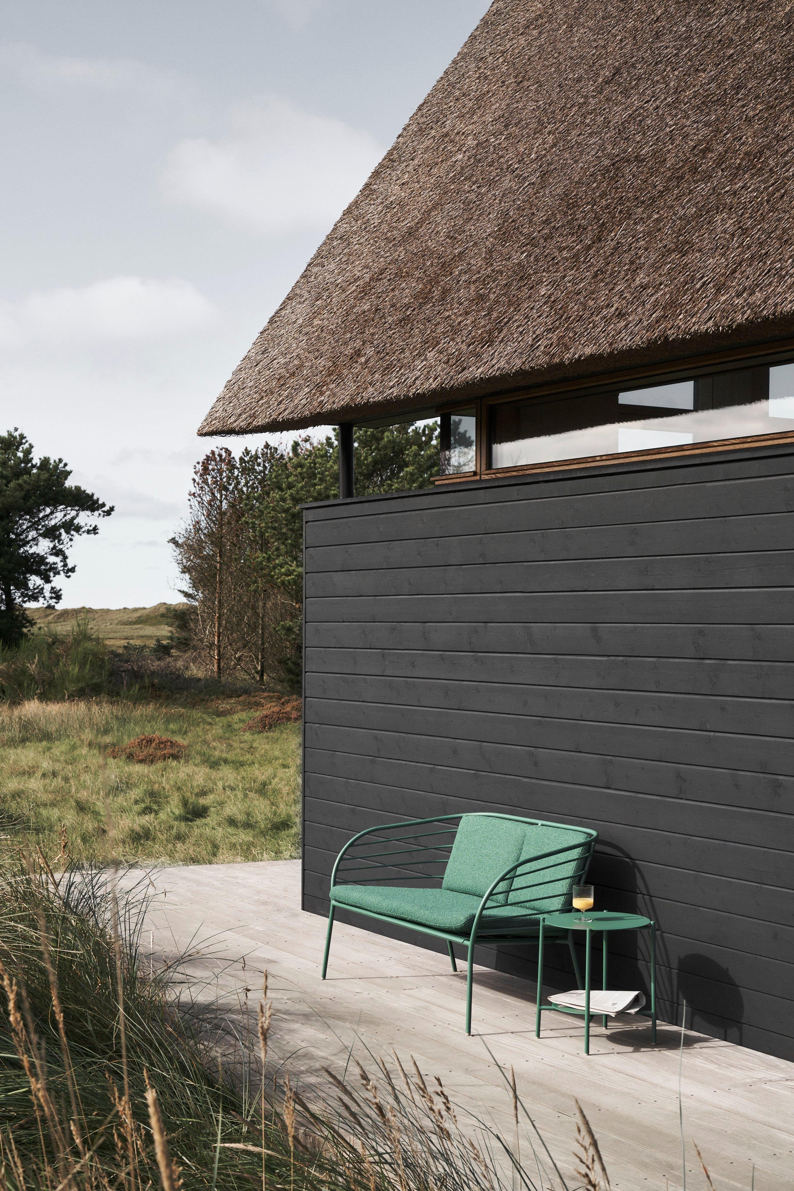 Two black lounge chairs on a wooden dock overlooking a calm lake, surrounded by dense green forest under a soft overcast sky.