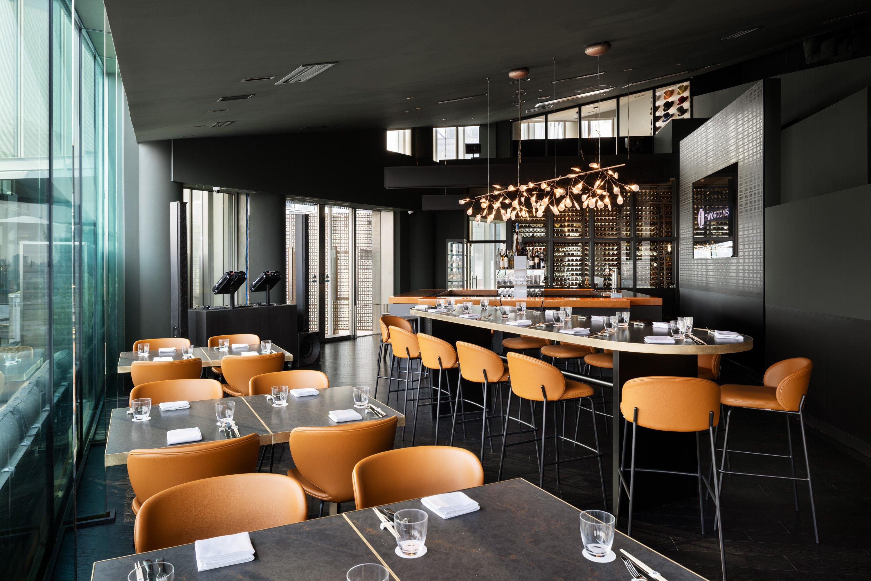 Restaurante moderno con sillas anaranjadas y mesas preparadas. Iluminación colgante decorativa.