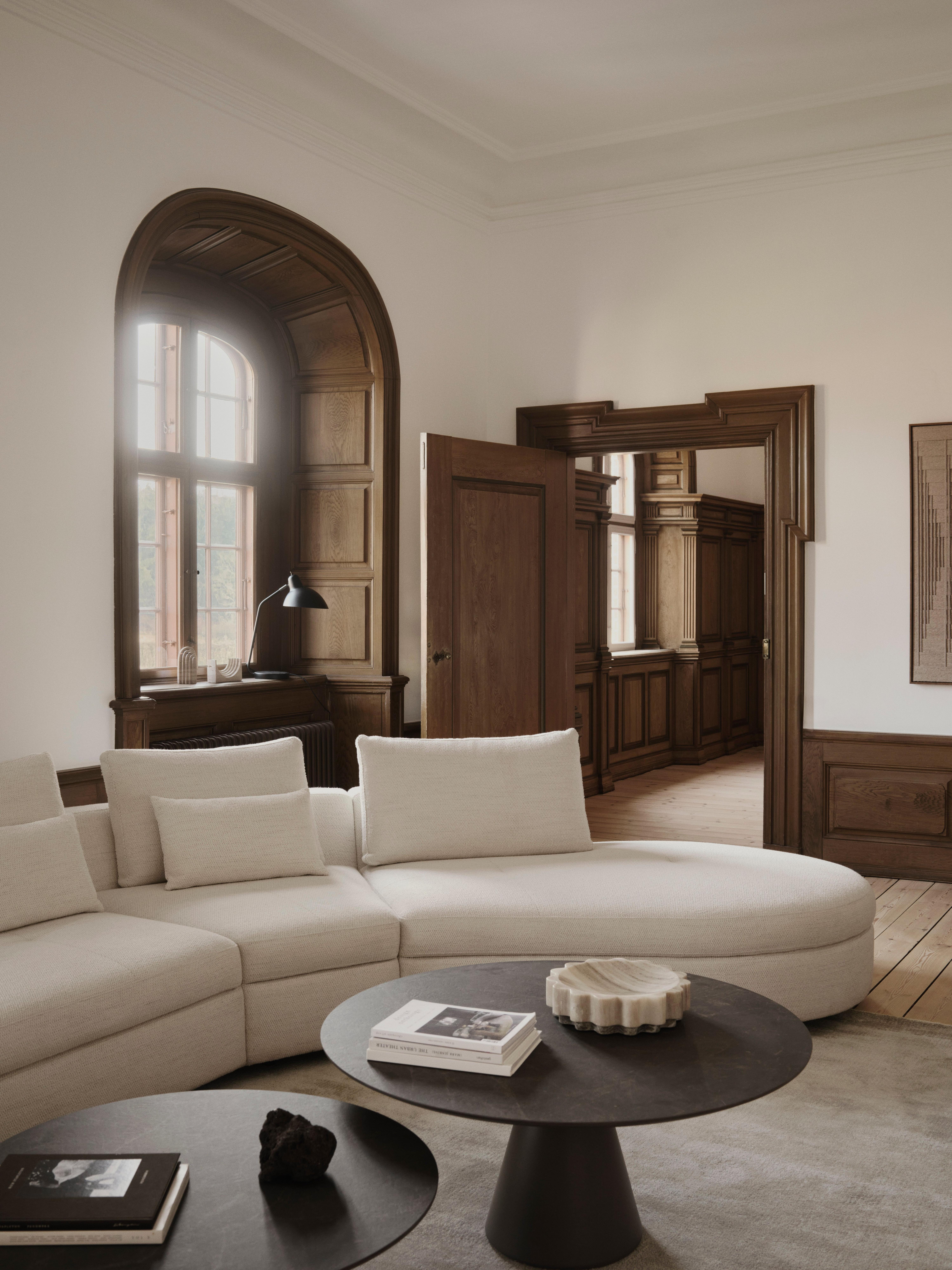 Beiges Ecksofa mit Kissen vor Rundtischen im Wohnzimmer mit Holzvertäfelung und Bogenfenster.