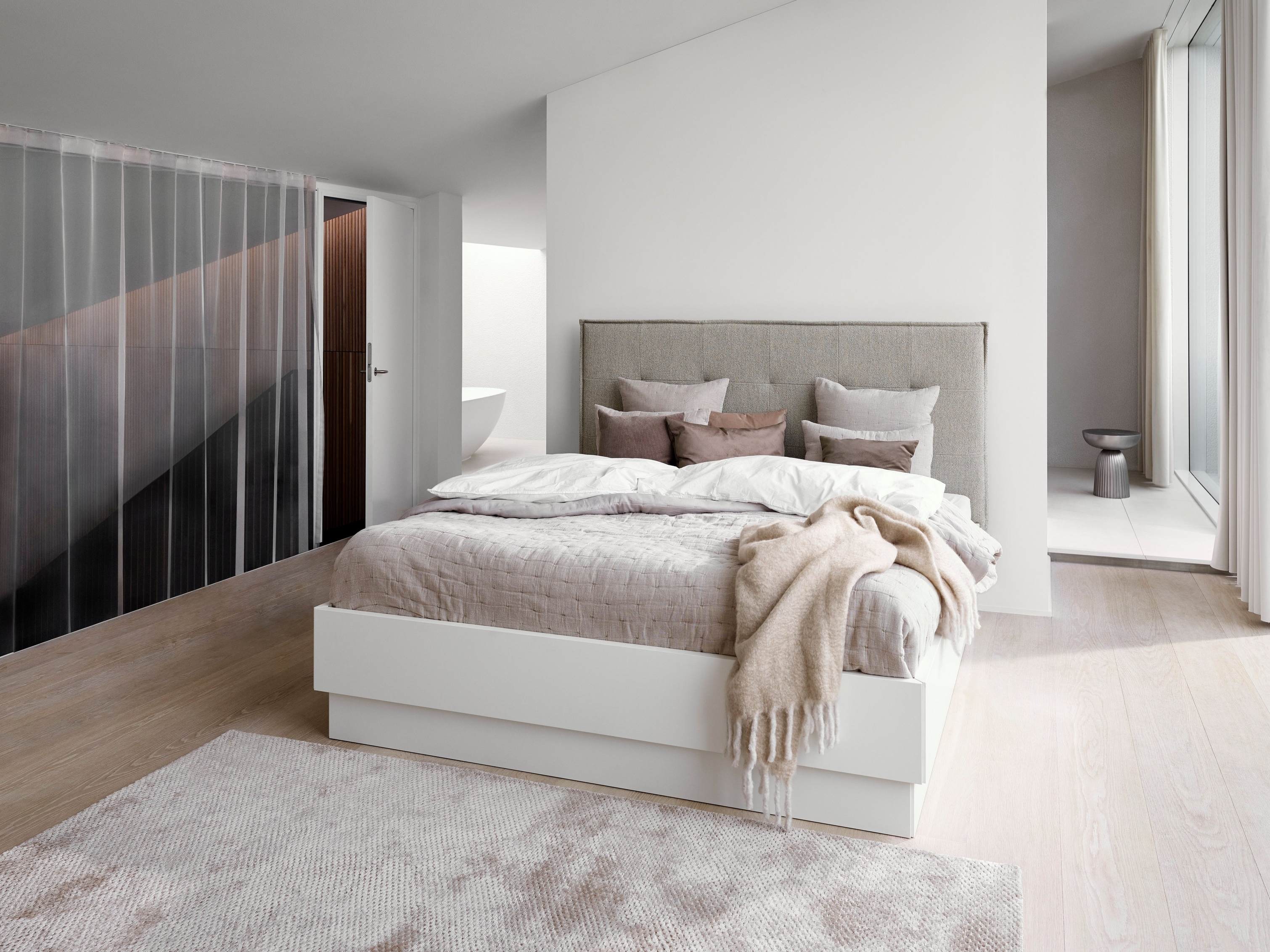 Minimalist bedroom with a grey upholstered bed, white linens, and a textured beige throw.