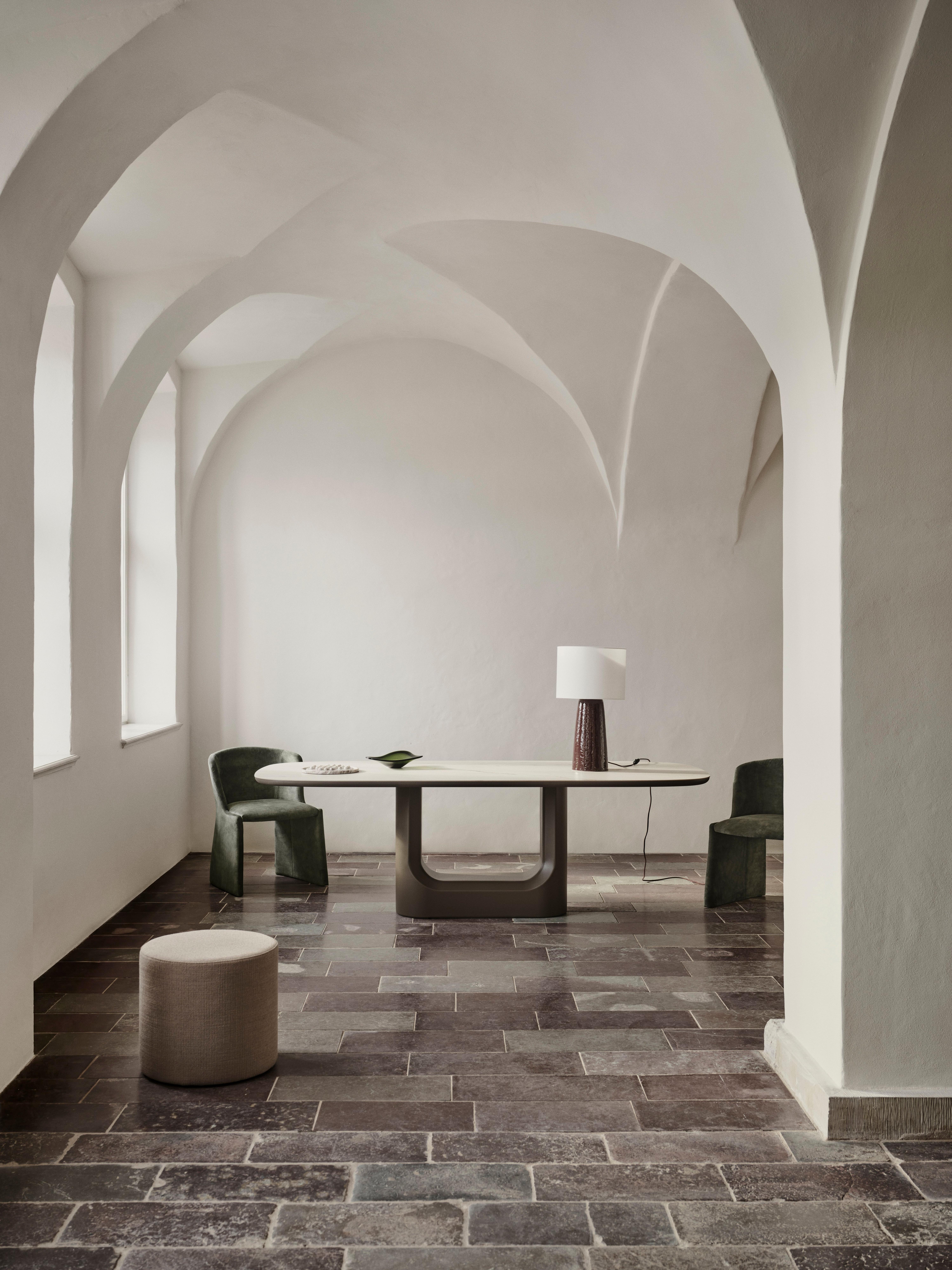Modern dining table with two green chairs, a table lamp and a small round ottoman.