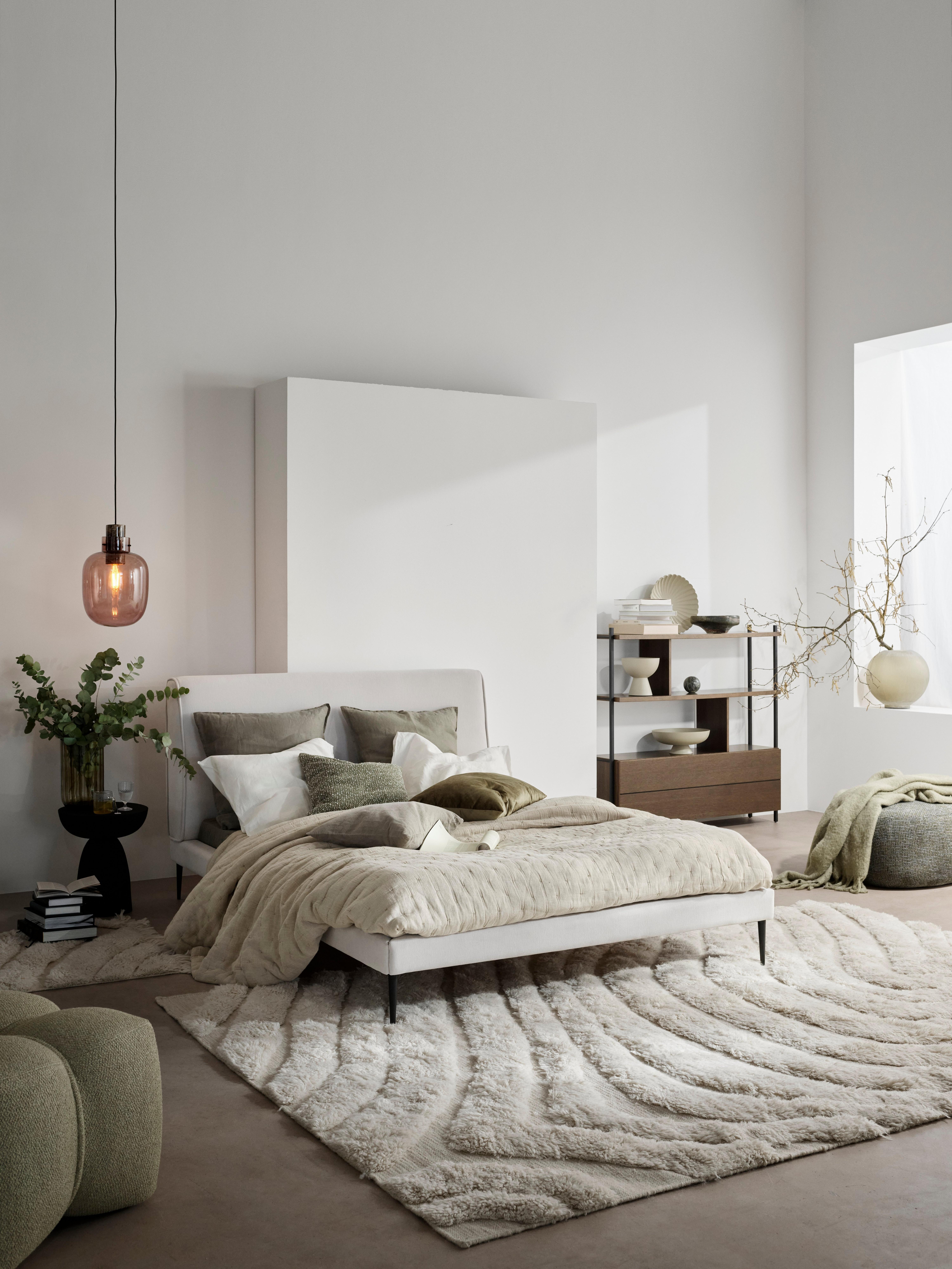 Modern bedroom with a beige Arlington bed, textured rug, pendant light, green Bermuda footstool, and open Calgary storage with decorative items.