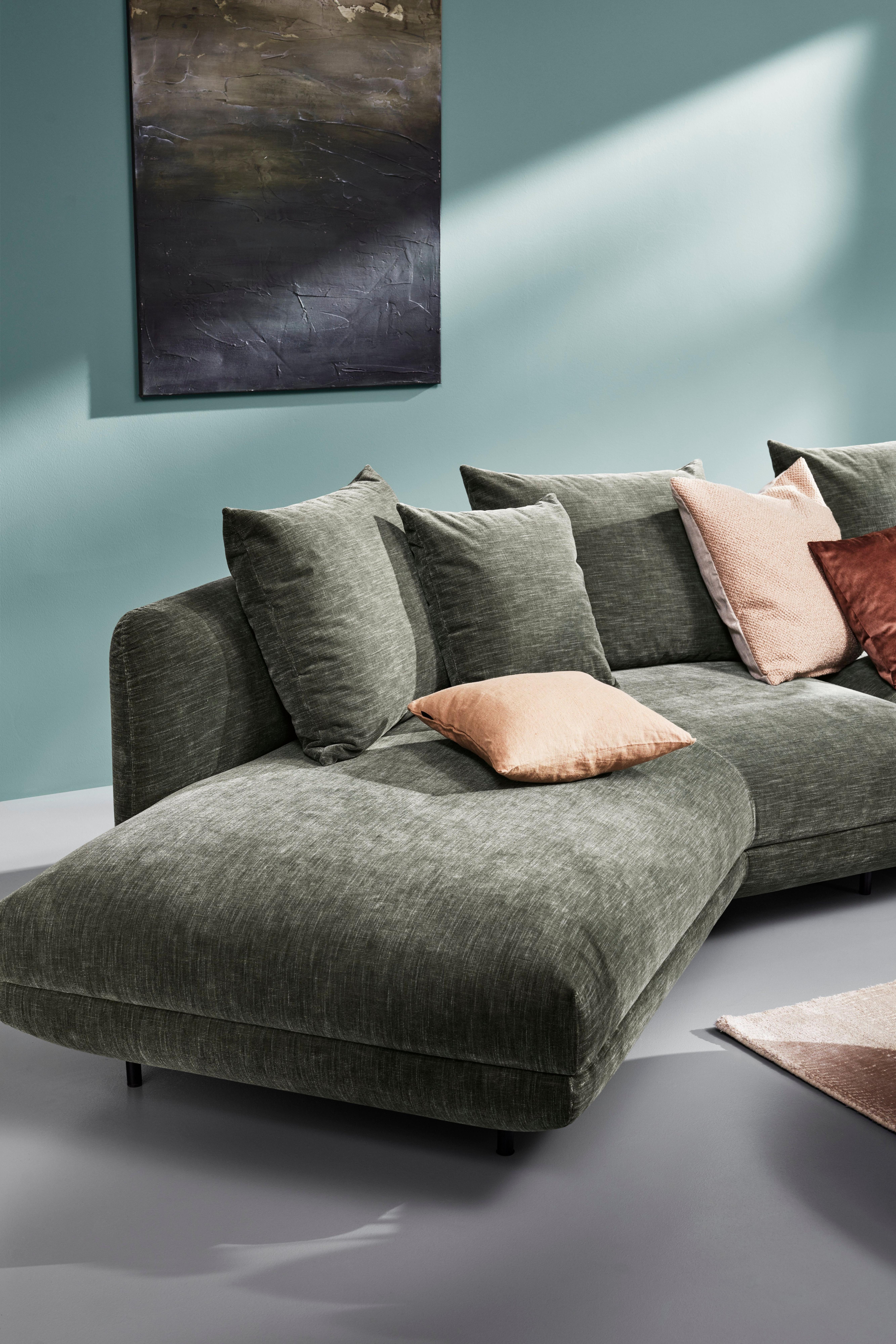 Le canapé sectionnel Salamanca vert avec des coussins contre un mur vert turquoise avec de l’art abstrait.