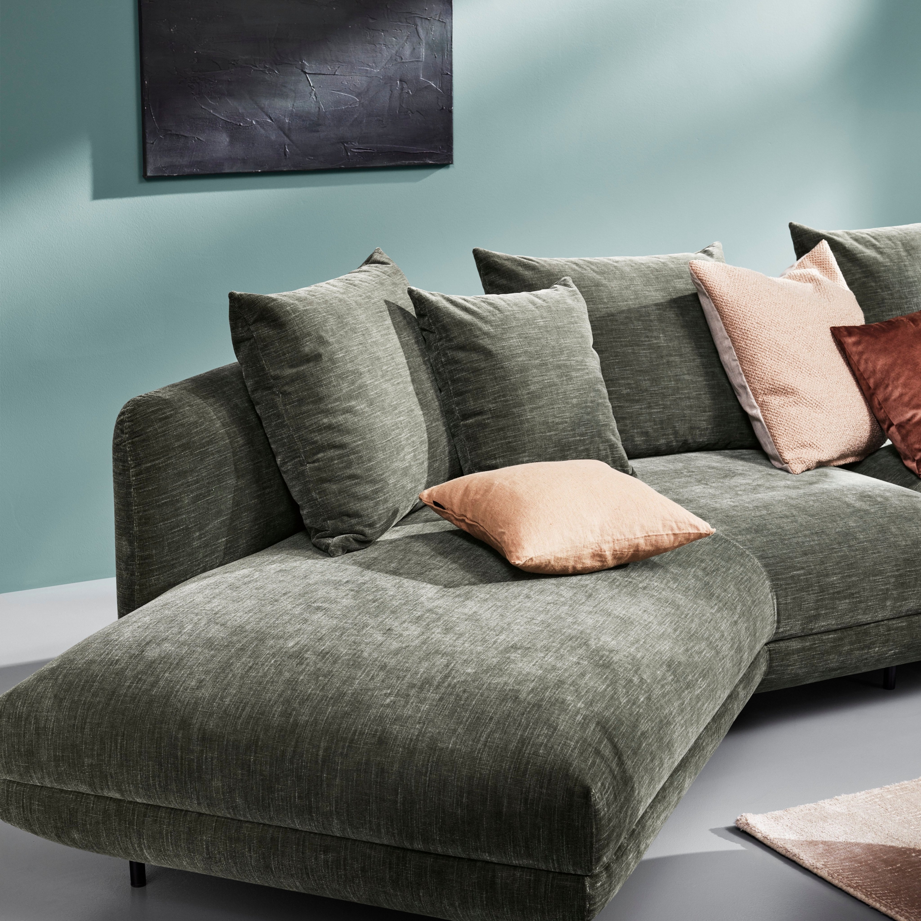 放着靠垫枕头的绿色 Salamanca 模块沙发，背景是以抽象艺术元素装饰的青绿色墙壁。
