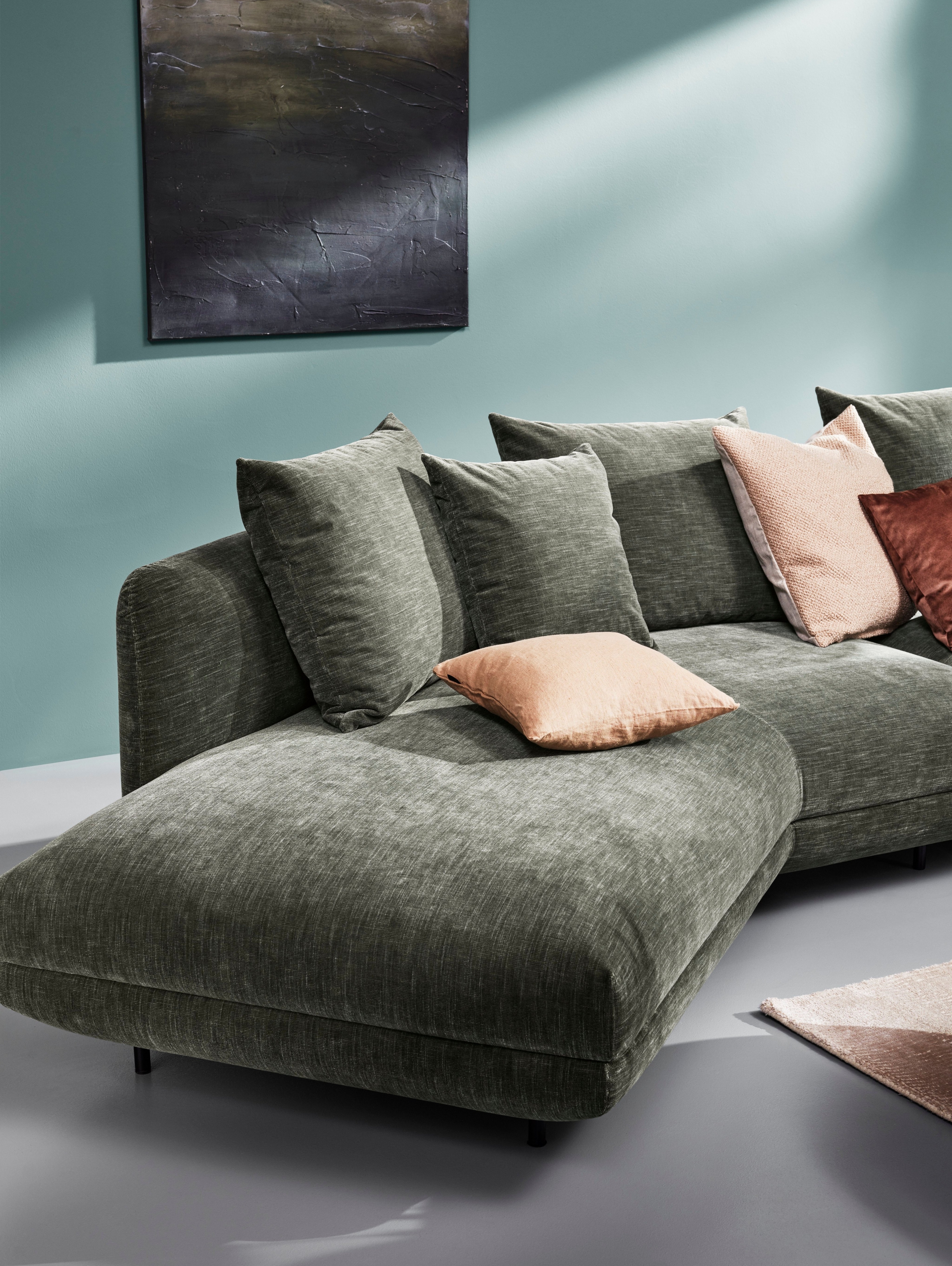 Green sectional Salamanca sofa with pillows against a teal wall with abstract art.