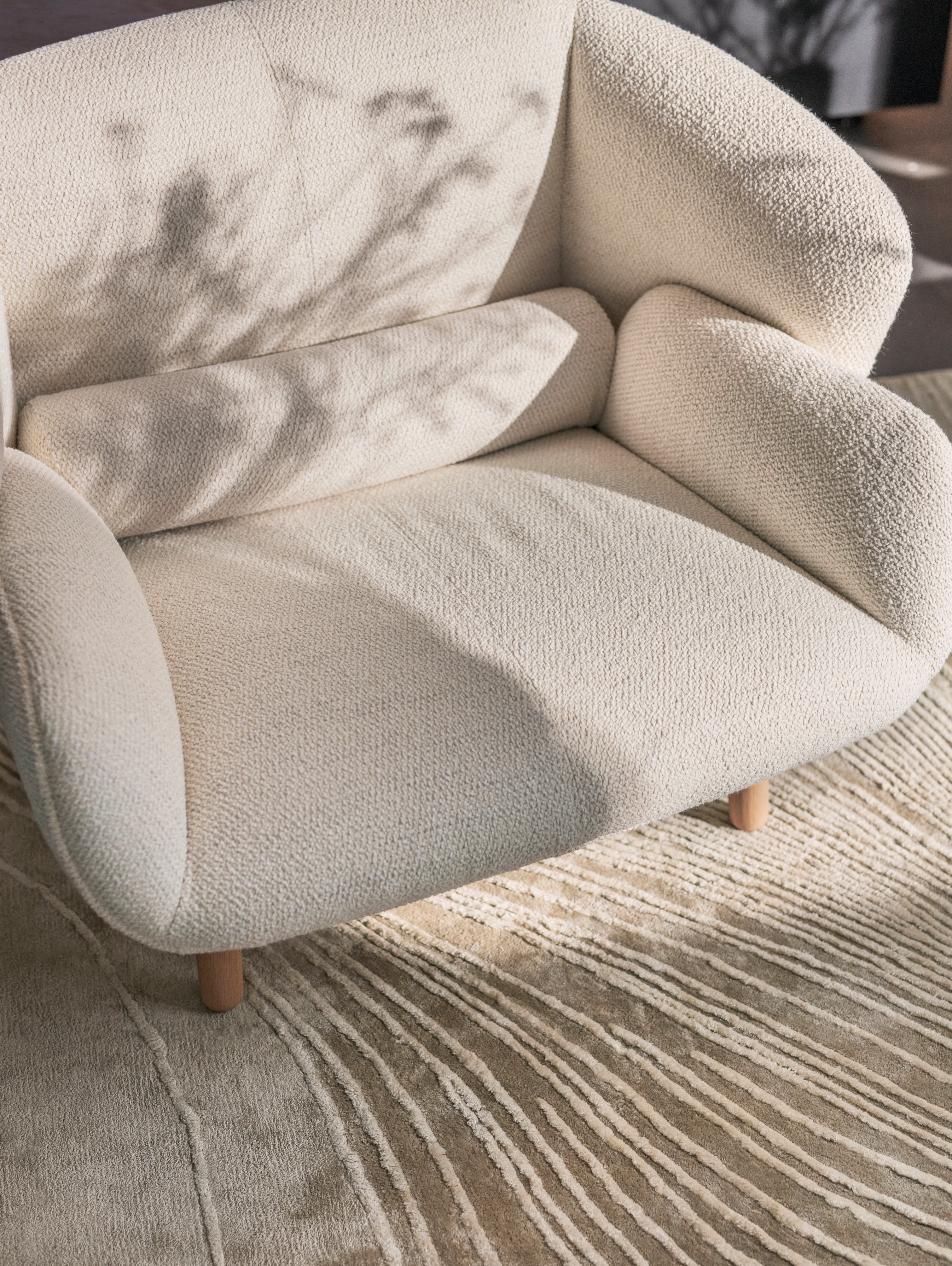 Fotel Fusion tapicerowany białą tkaniną Lazio w połączeniu z dywanem Tide w kolorze szaro-białym.