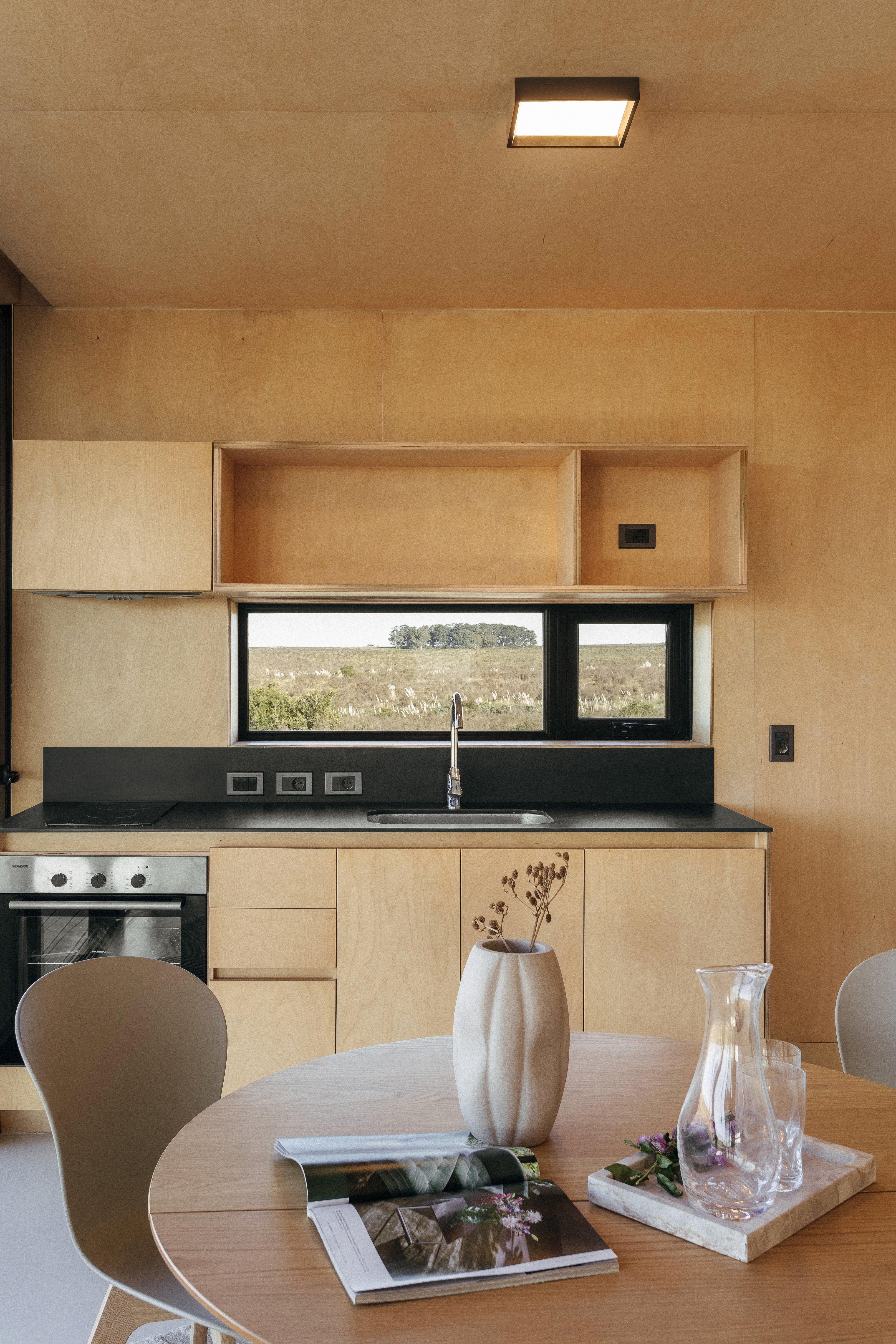 現代廚房，木質櫥櫃，窗外景色，圓桌上有花瓶和書。