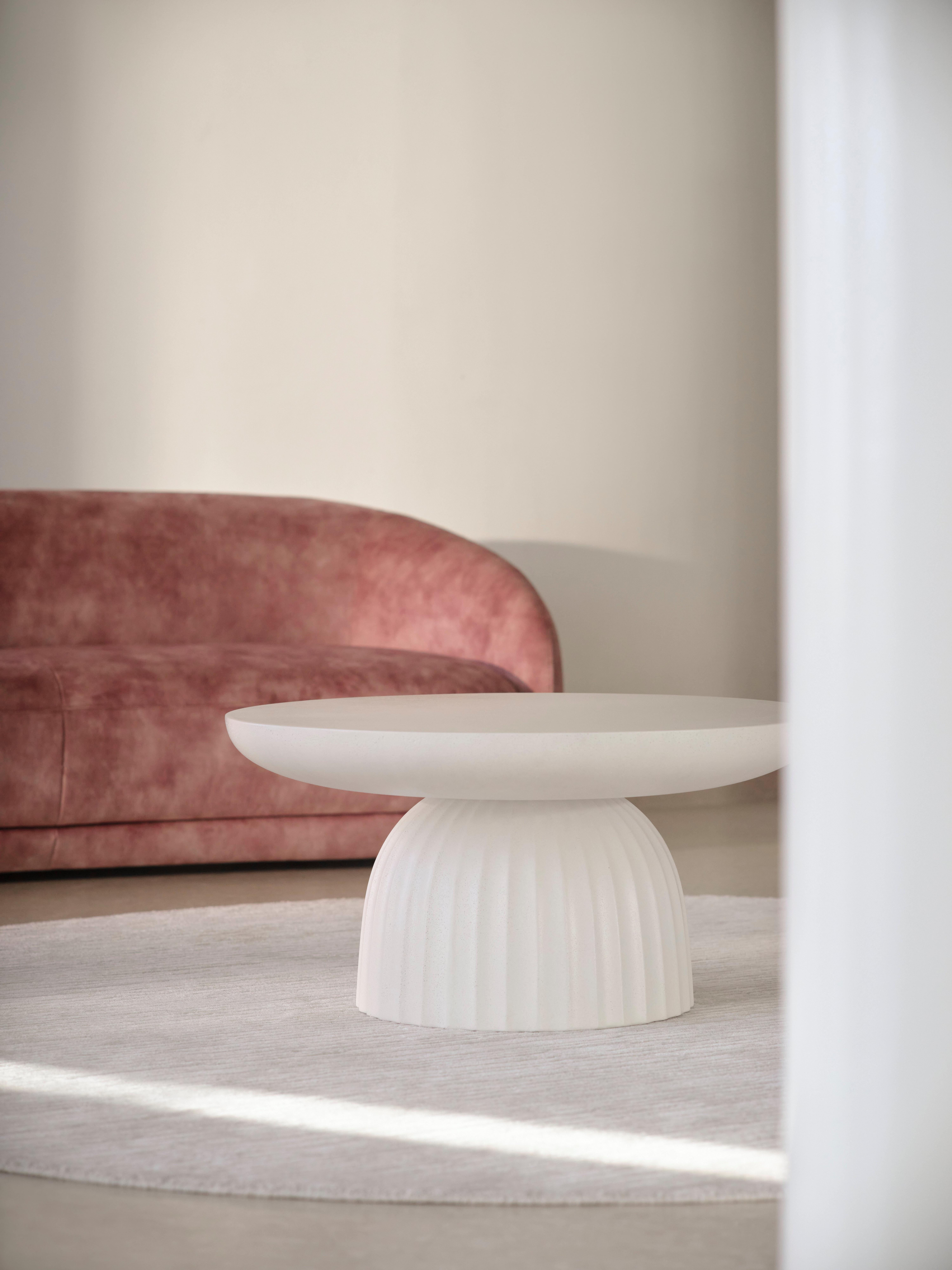 Minimalist room with a white sculptural coffee table on a round rug, set in front of a curved dusty pink velvet sofa.