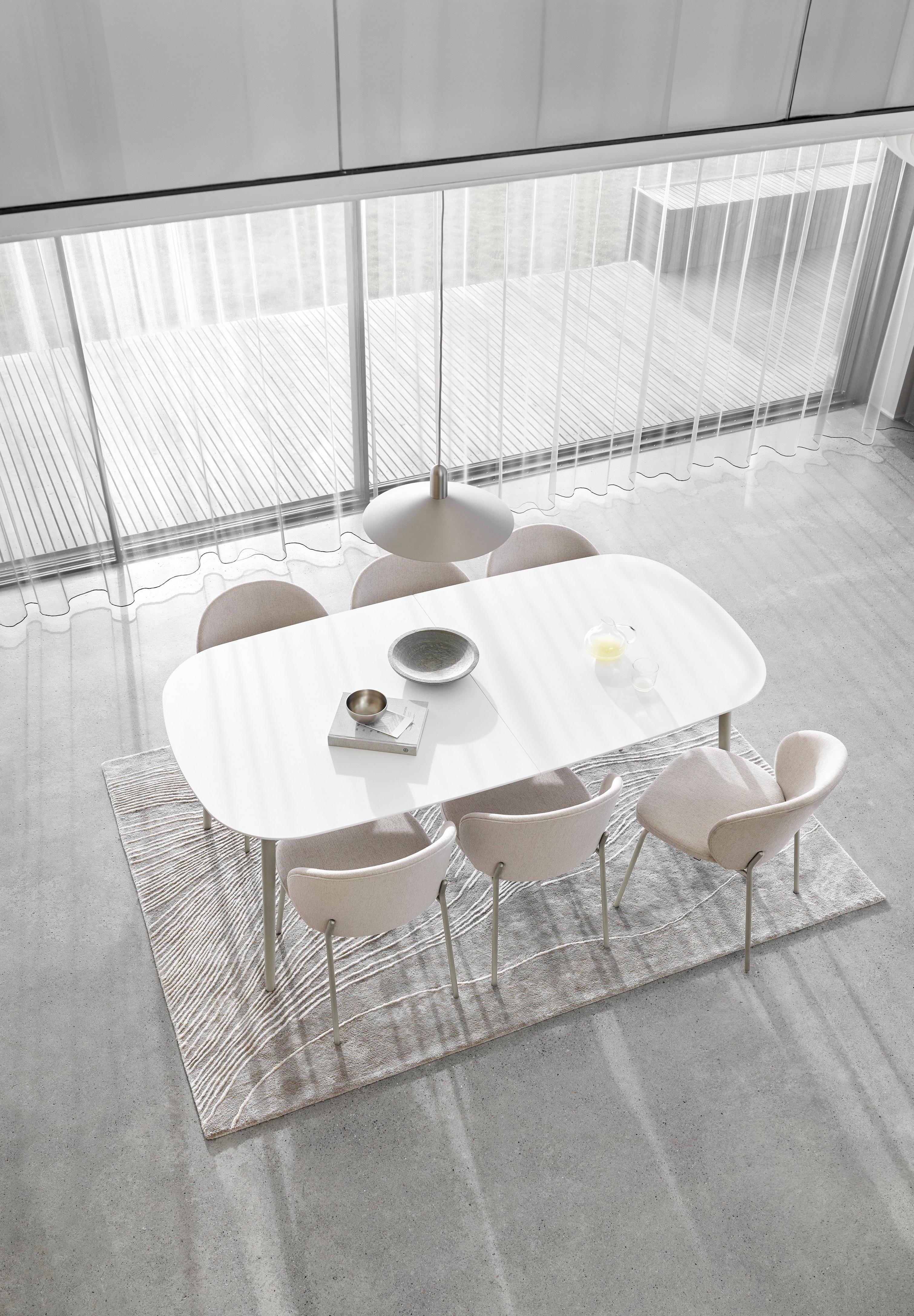 Sala de jantar minimalista com mesa oval branca, cadeiras, cortinas transparentes e tapete texturizado.