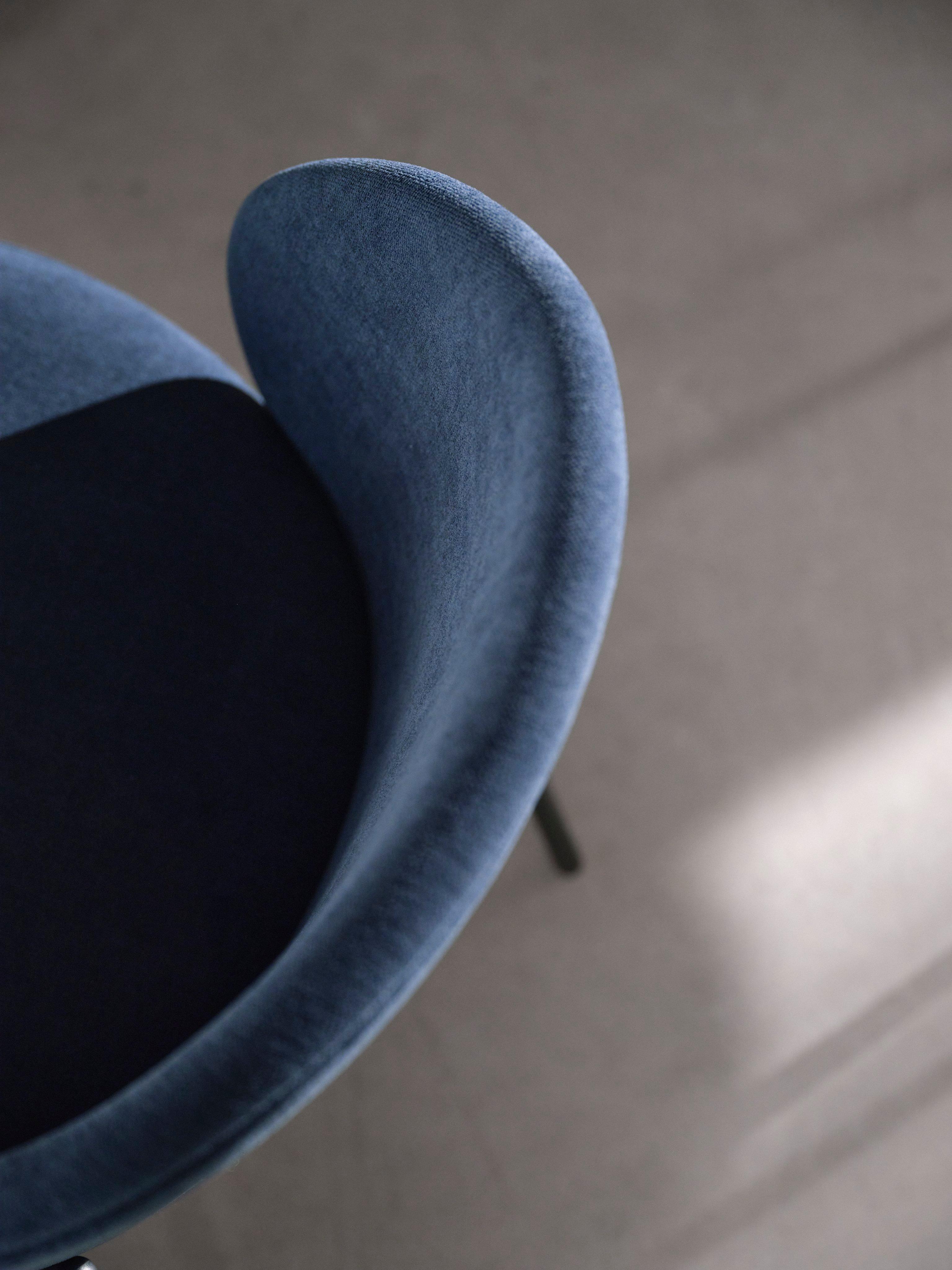 Nahaufnahme eines blauen Princeton Stuhls mit geschwungener Rückenlehne und schwarzem Sitzkissen auf einem hellen Boden.