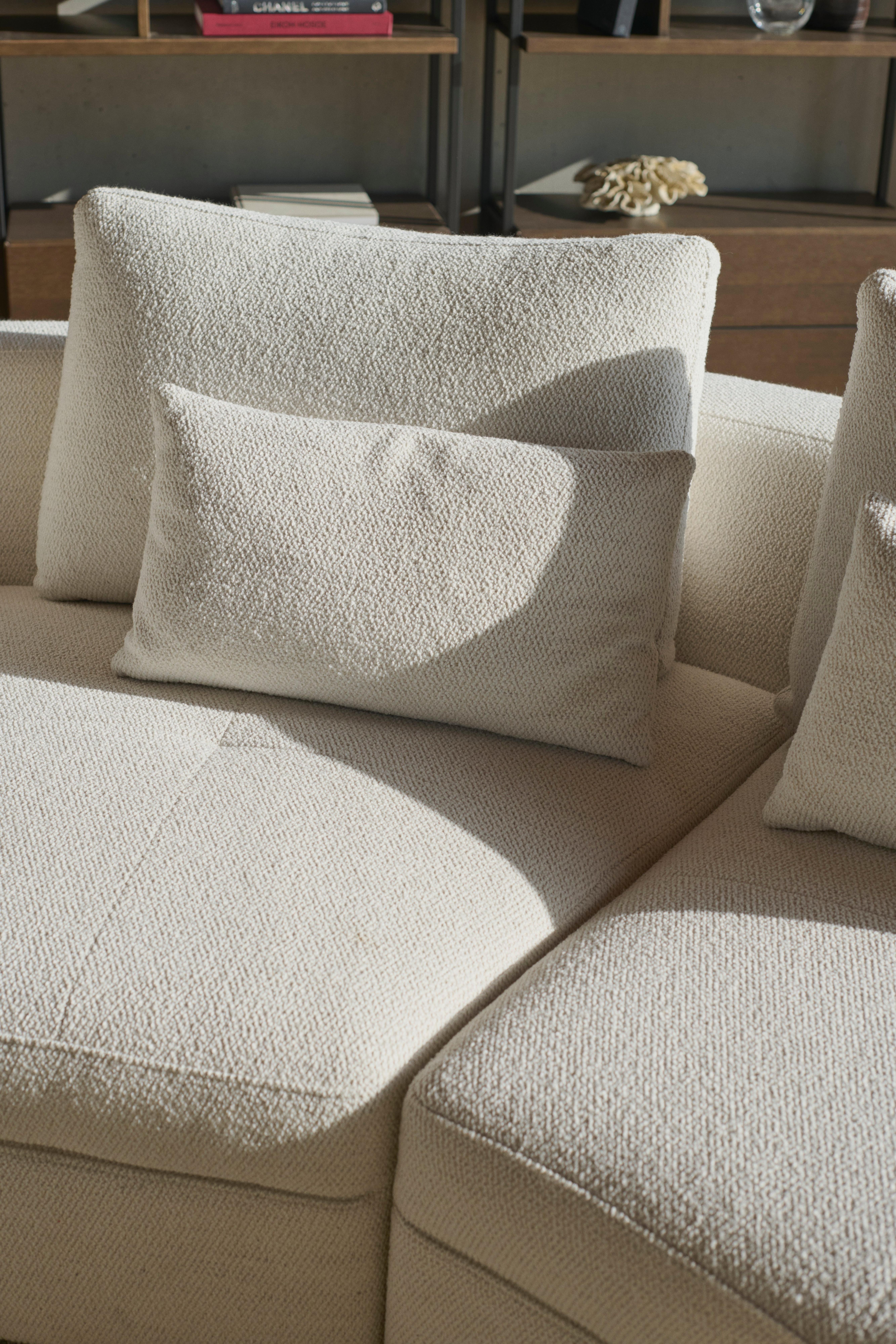 Bergamo sofa with round lounging unit in white Lazio fabric, with the Bergamo deco cushions in white Lazio fabric, the Calgary storage with drawer in dark oak veneer and the Bali sculpture in natural color.