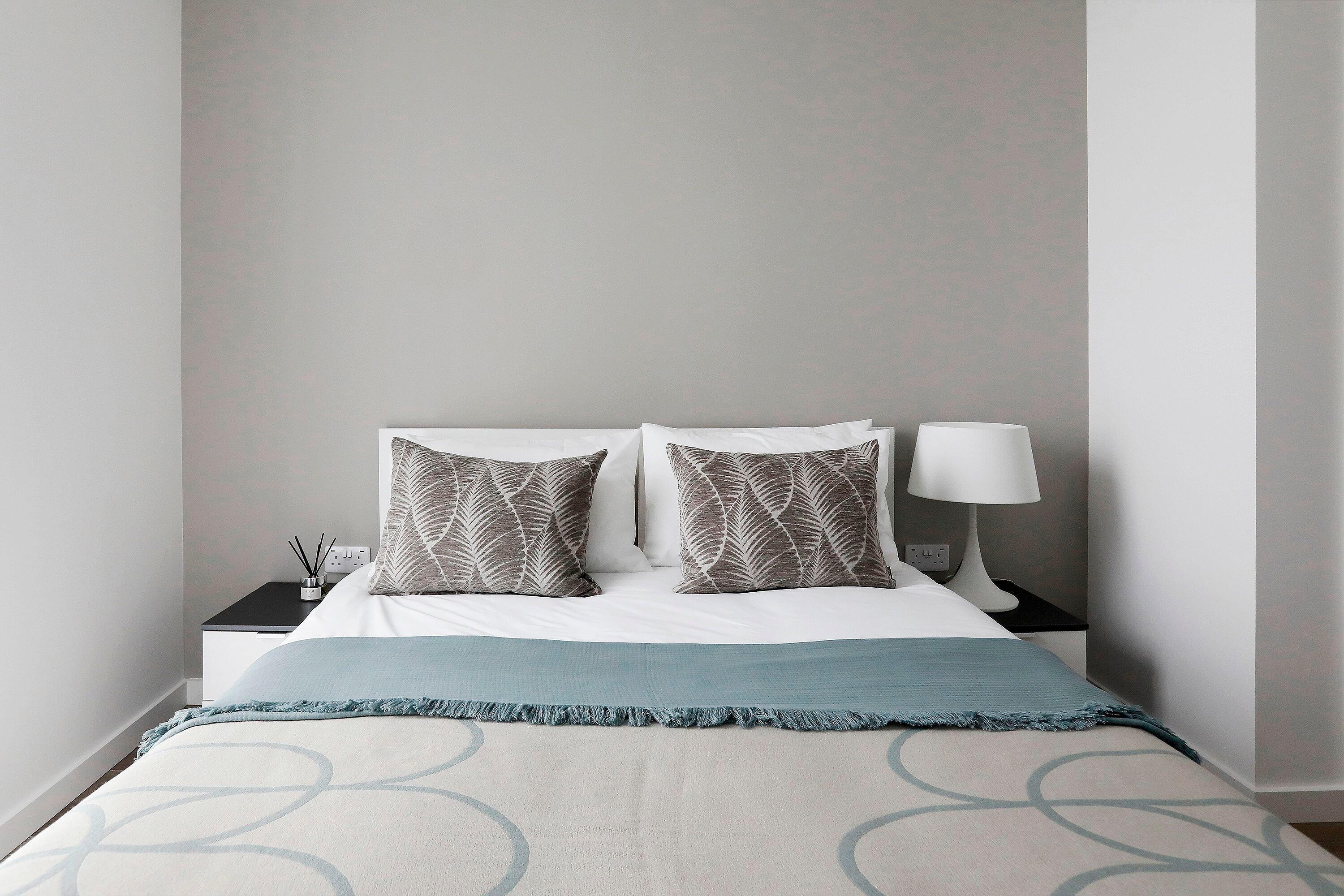 Minimalist bedroom with patterned pillows and a textured throw on the bed.