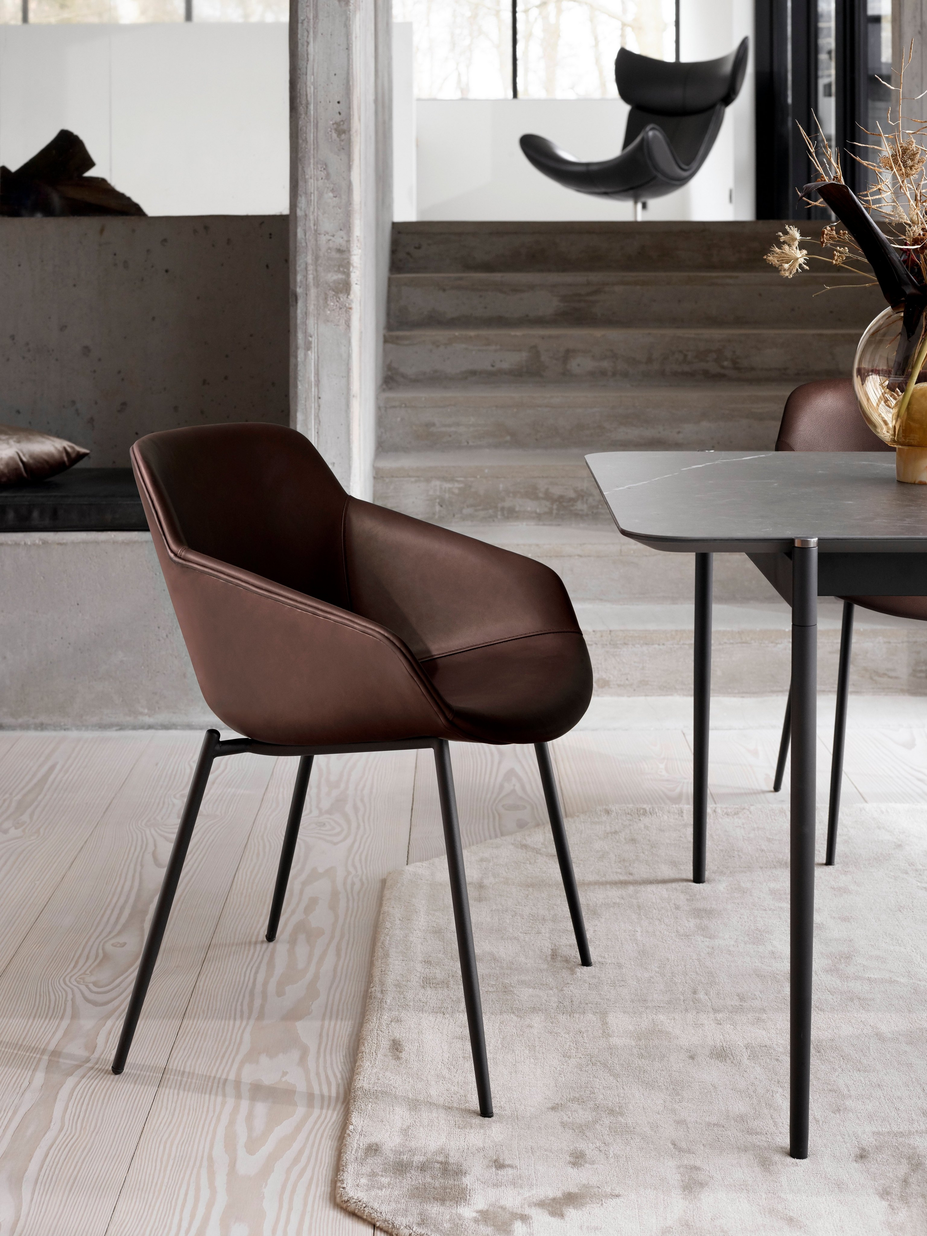 Leather dining chair with black legs, near a table with a vase, in a modern setting.