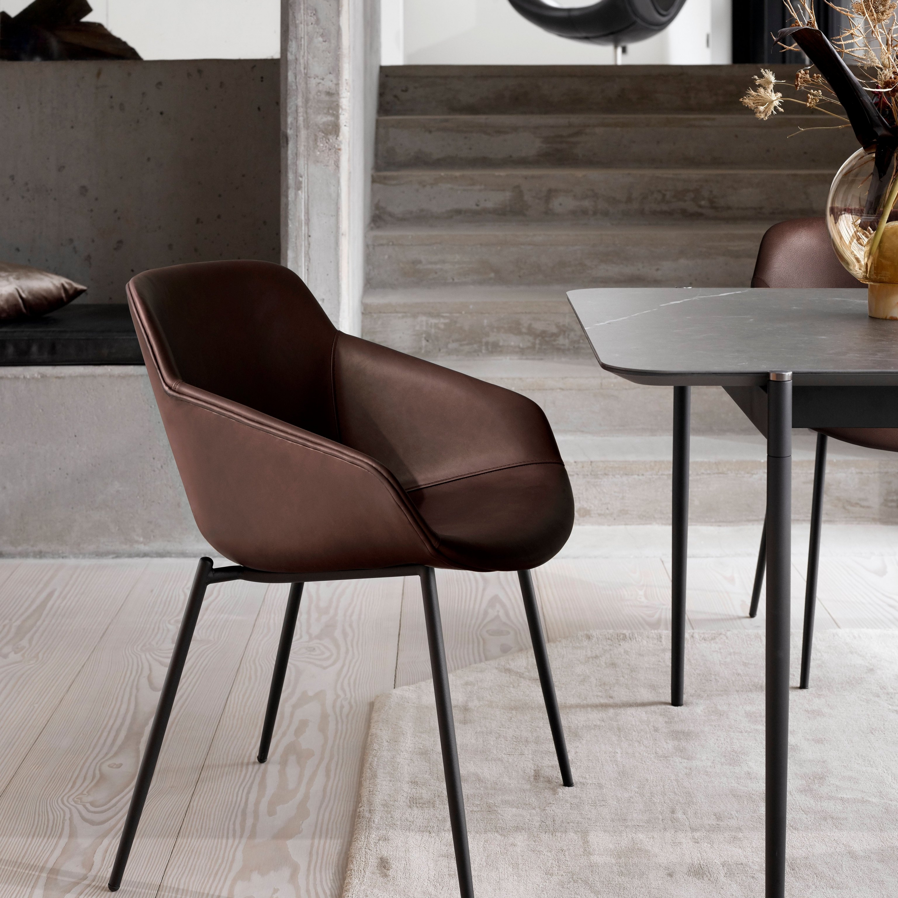 Nahkainen ruokapöydän tuoli mustilla jaloilla, lähellä pöytä ja maljakko modernissa ympäristössä.