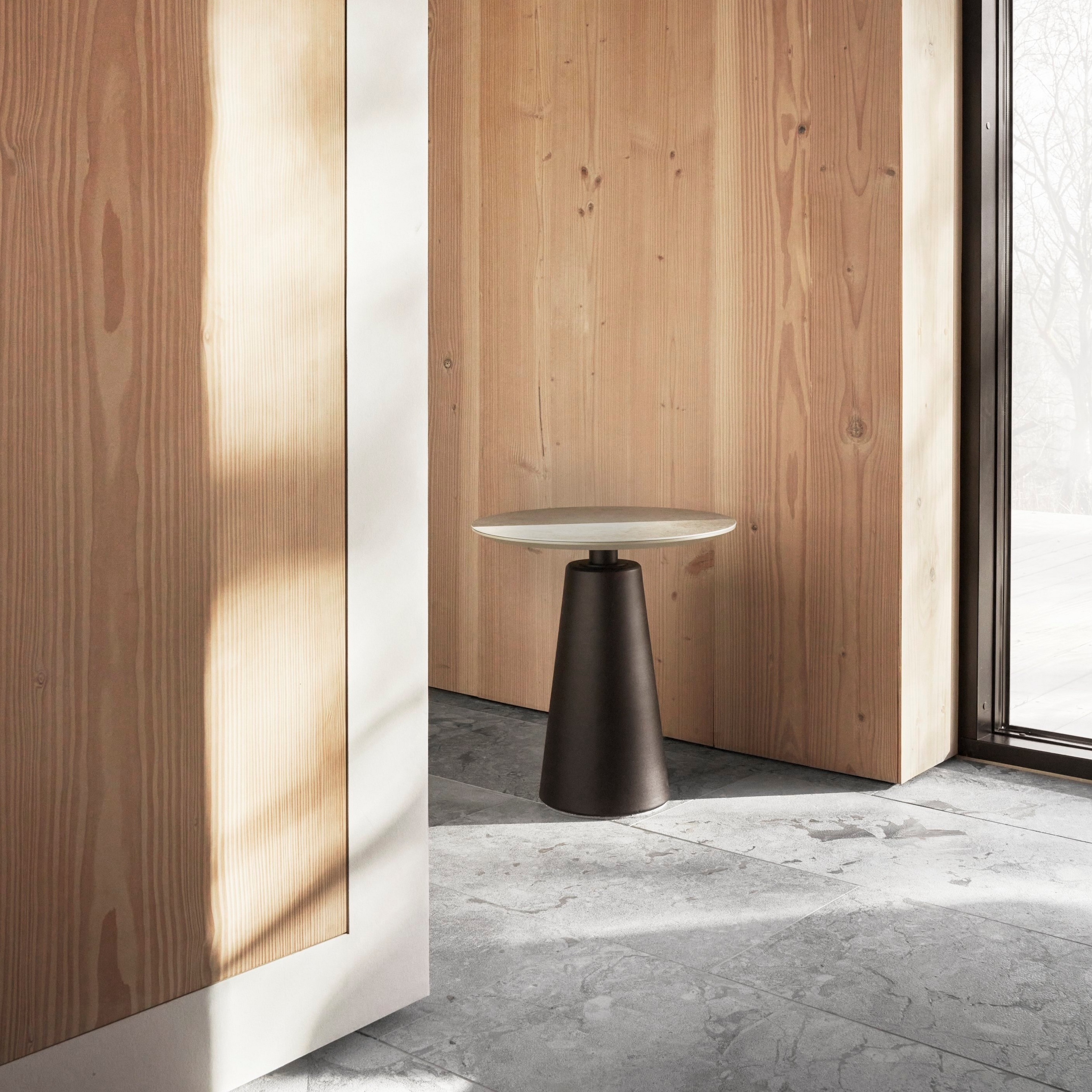 Minimalistyczna przestrzeń z drewnianymi ścianami, prostym stolikiem pomocniczym i naturalnym światłem wpadającym przez duże okna.