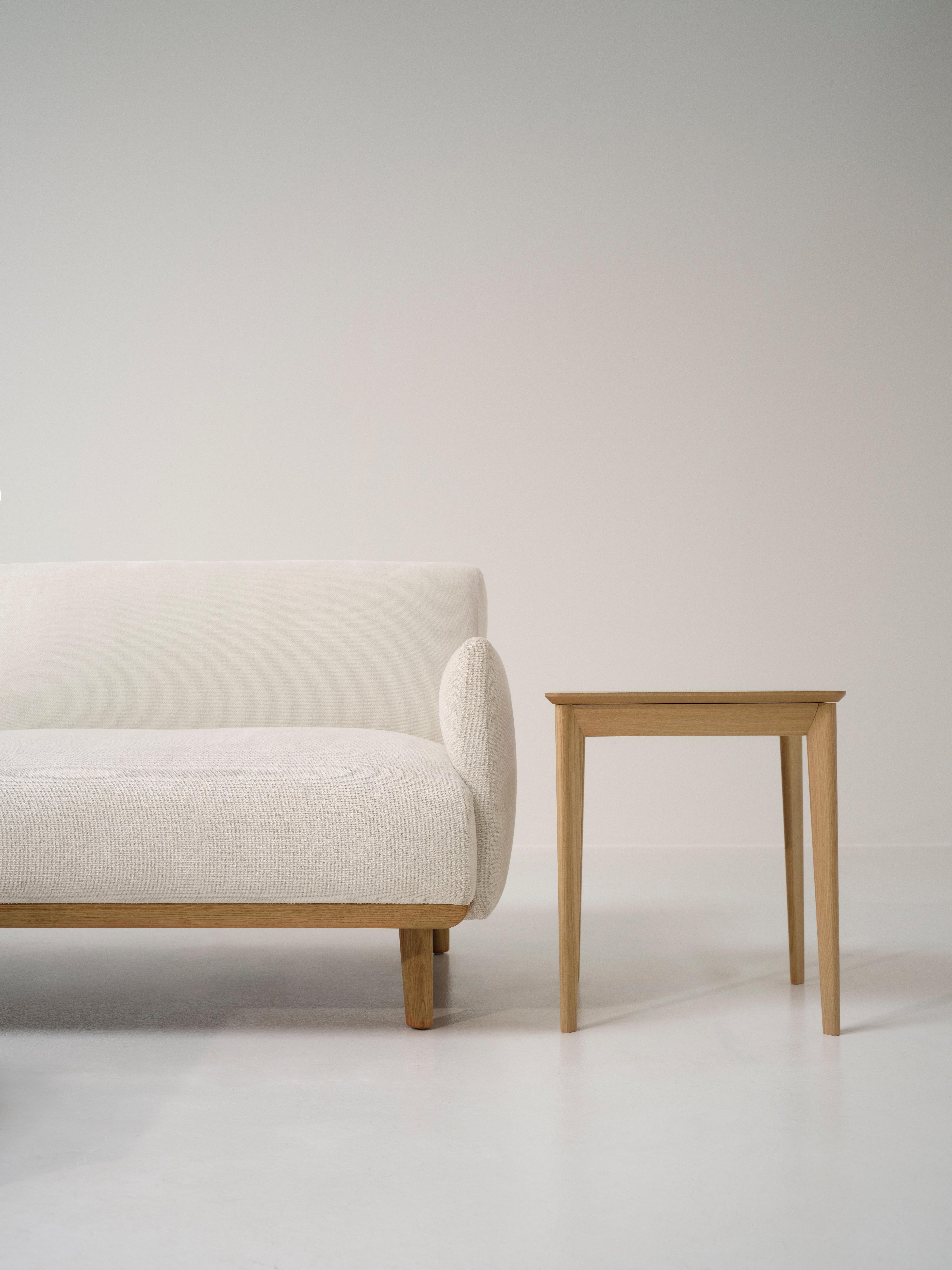 Light wood-framed white sofa next to a matching square side table, set against a pale wall and seamless light floor.