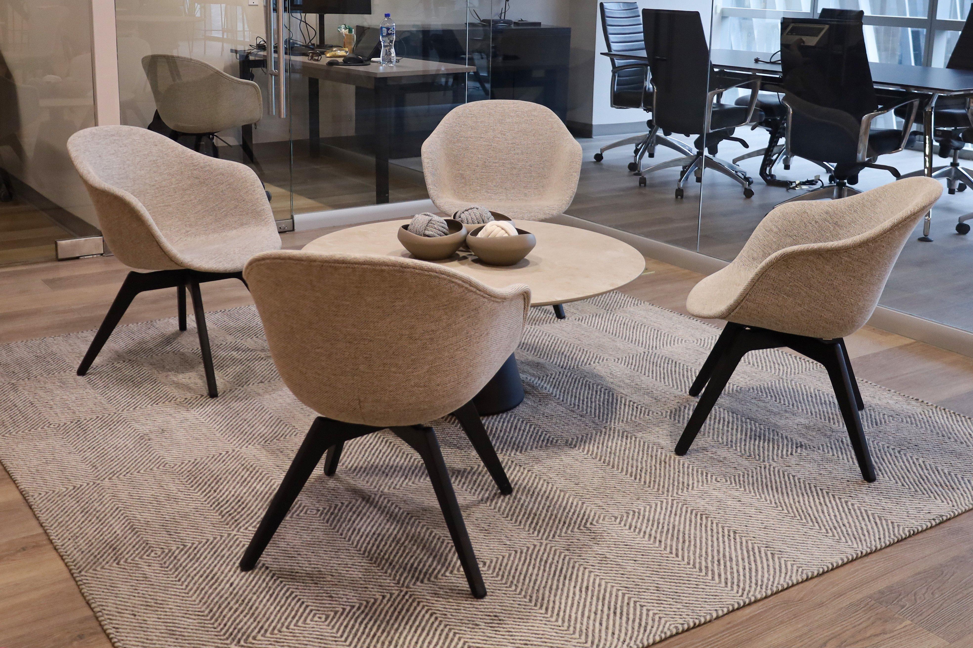 Four beige chairs around a round table with decorative bowls on a patterned rug.