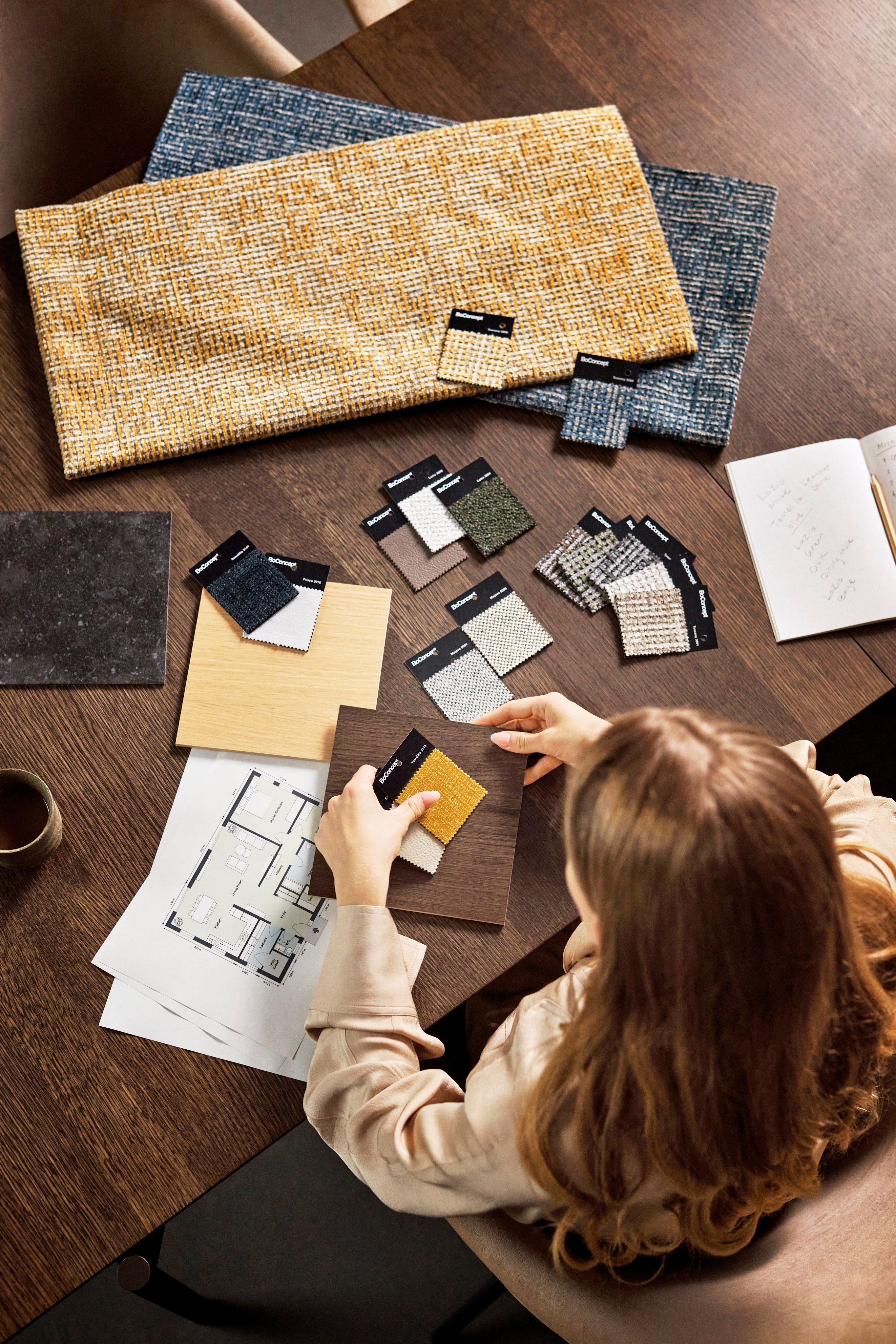 Diseñador eligiendo muestras de tela en una mesa de madera con plano de piso y notas.