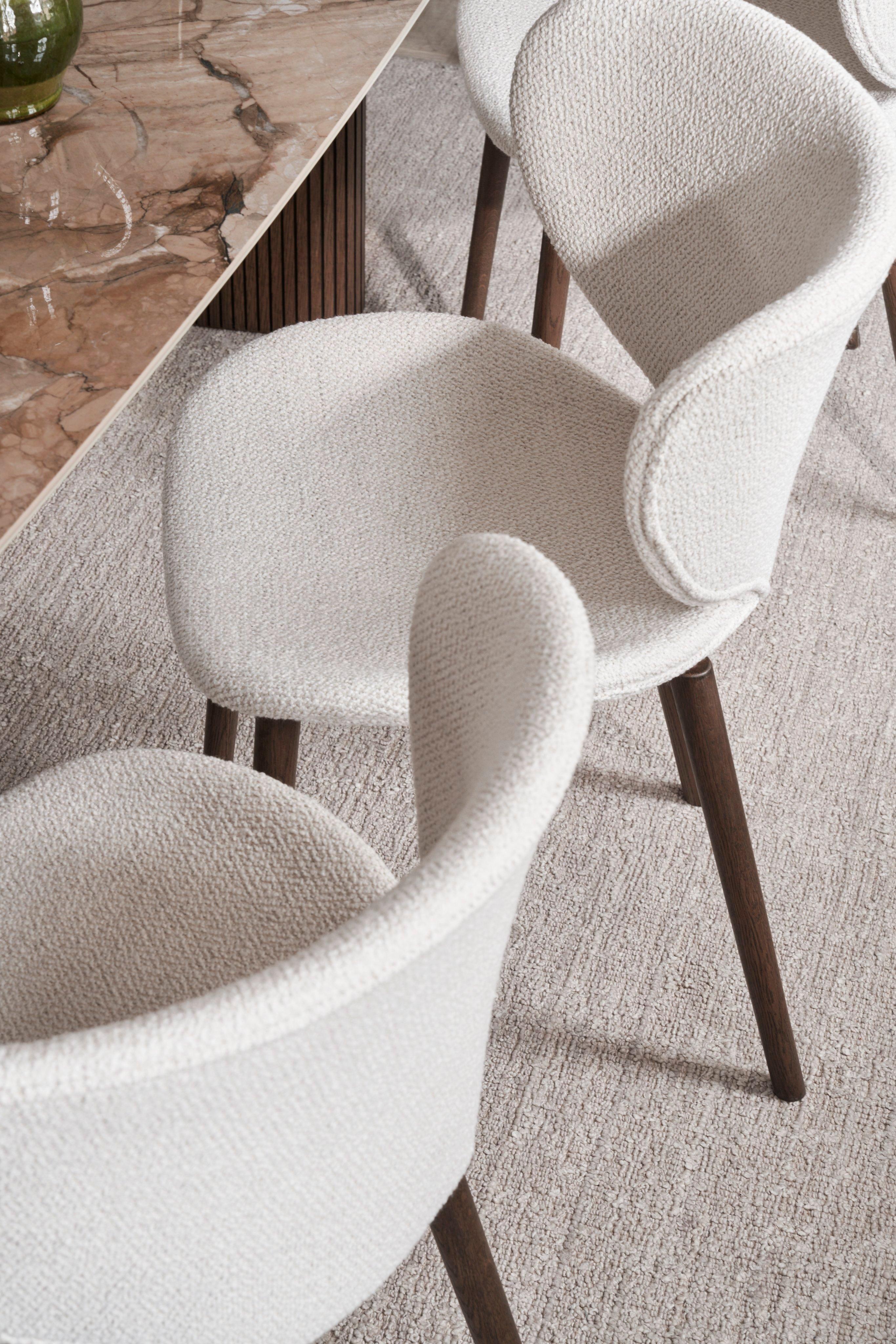 Cream textured chairs with wooden legs beside a marble table.
