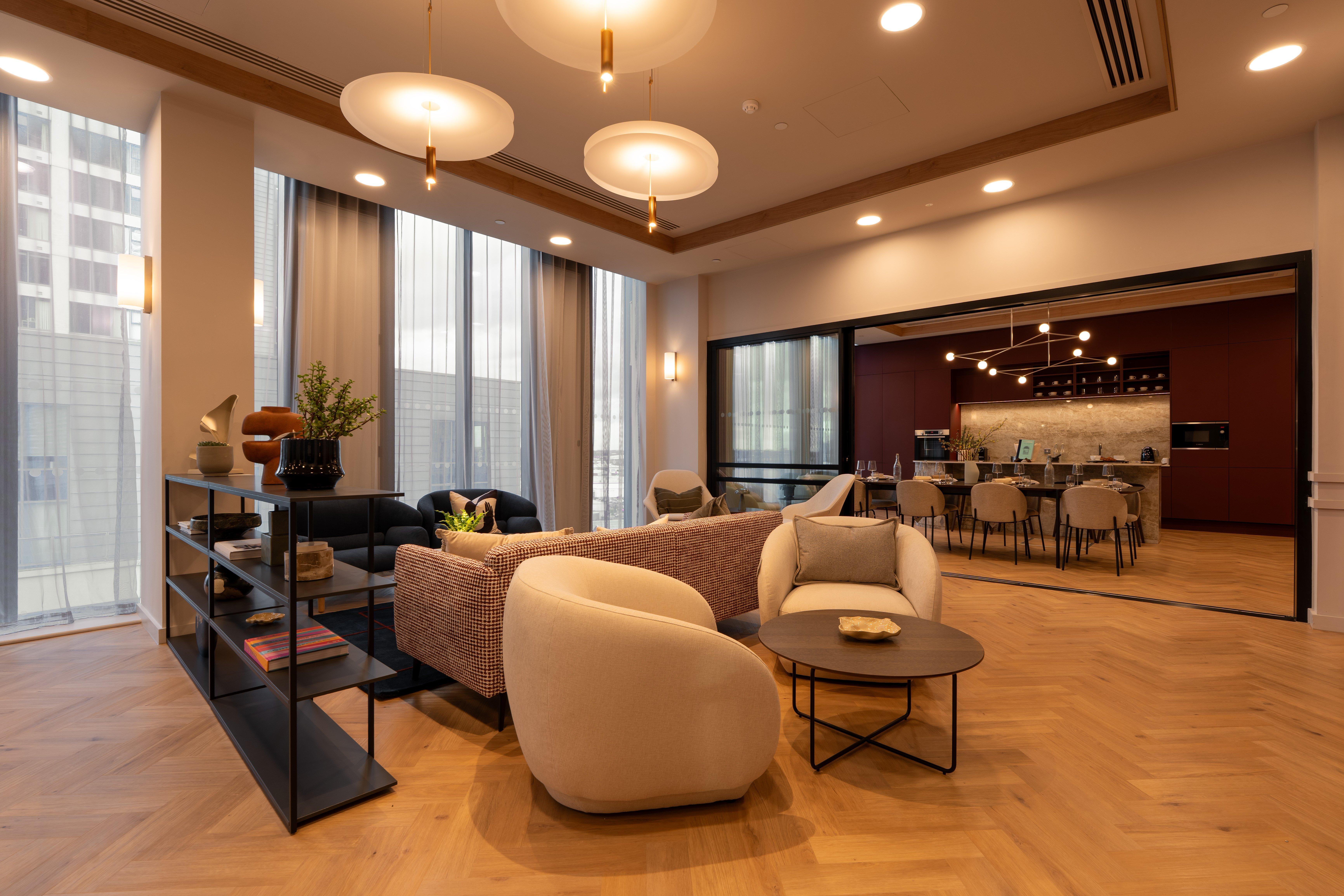 Salón moderno con sofá, sillones y mesa baja, junto a comedor y cocina abierta.