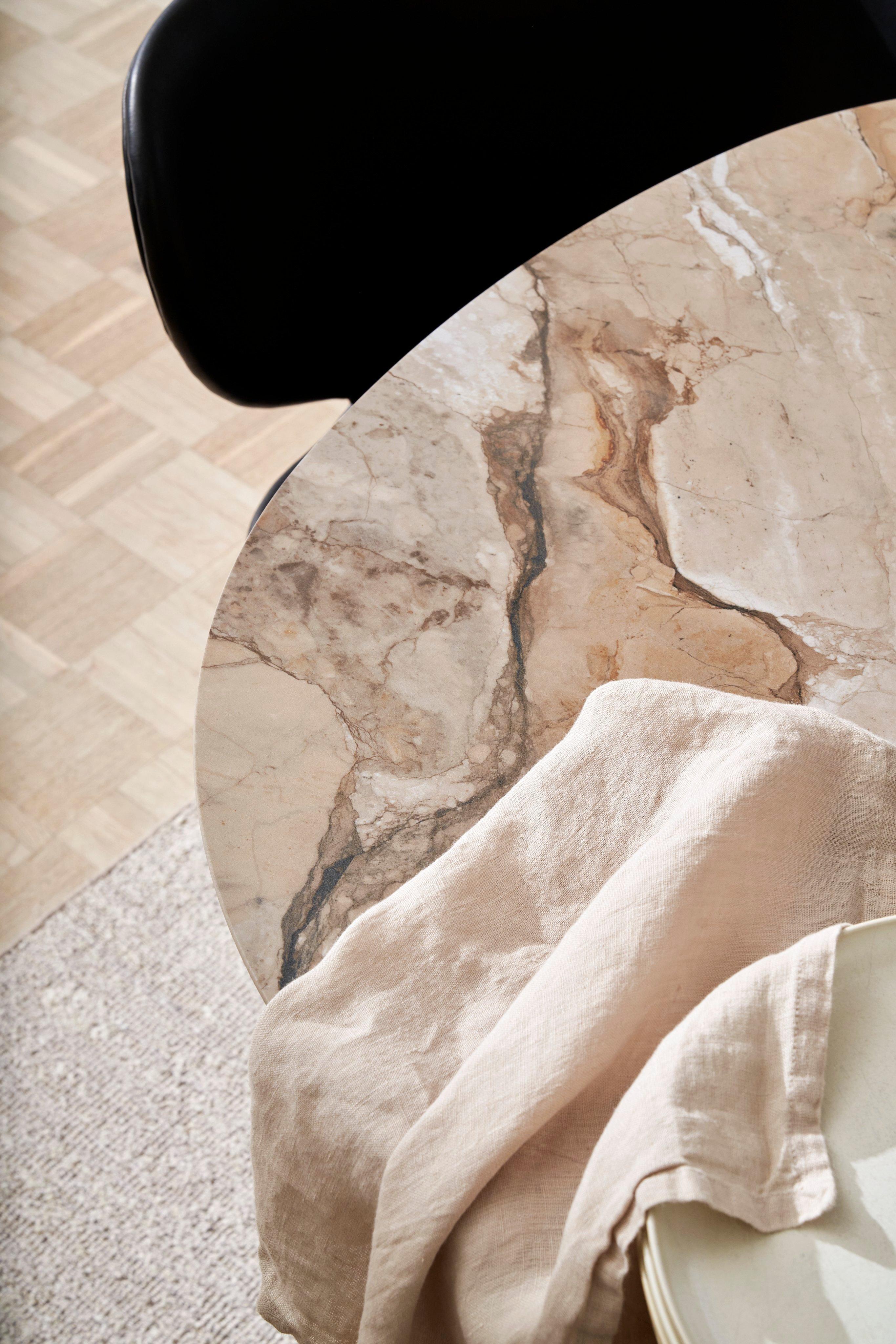 Marble tabletop with beige cloth draped over, next to a black chair and light floor.