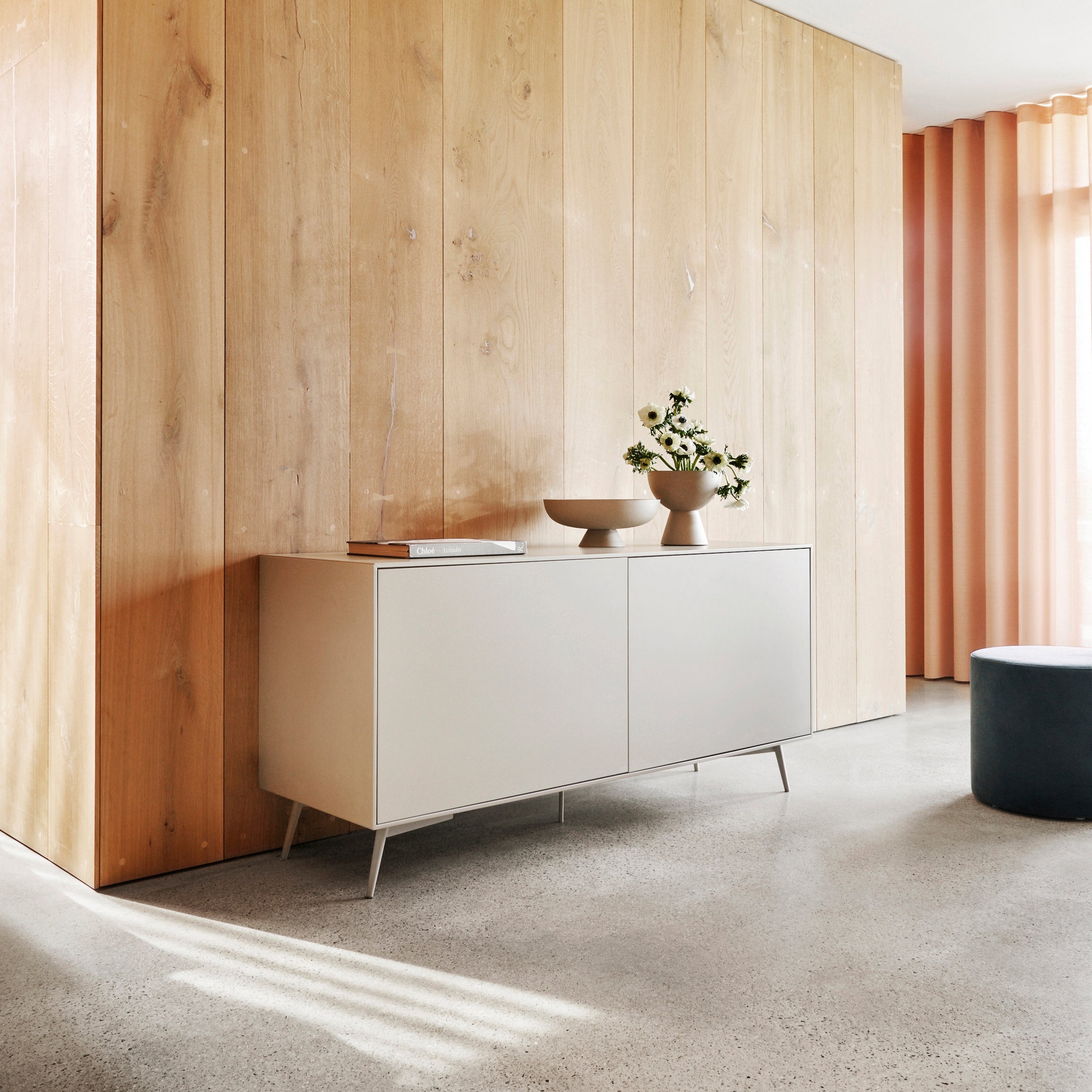 Modern sideboard with decor against a wooden wall, floor-to-ceiling curtains, in a bright room.