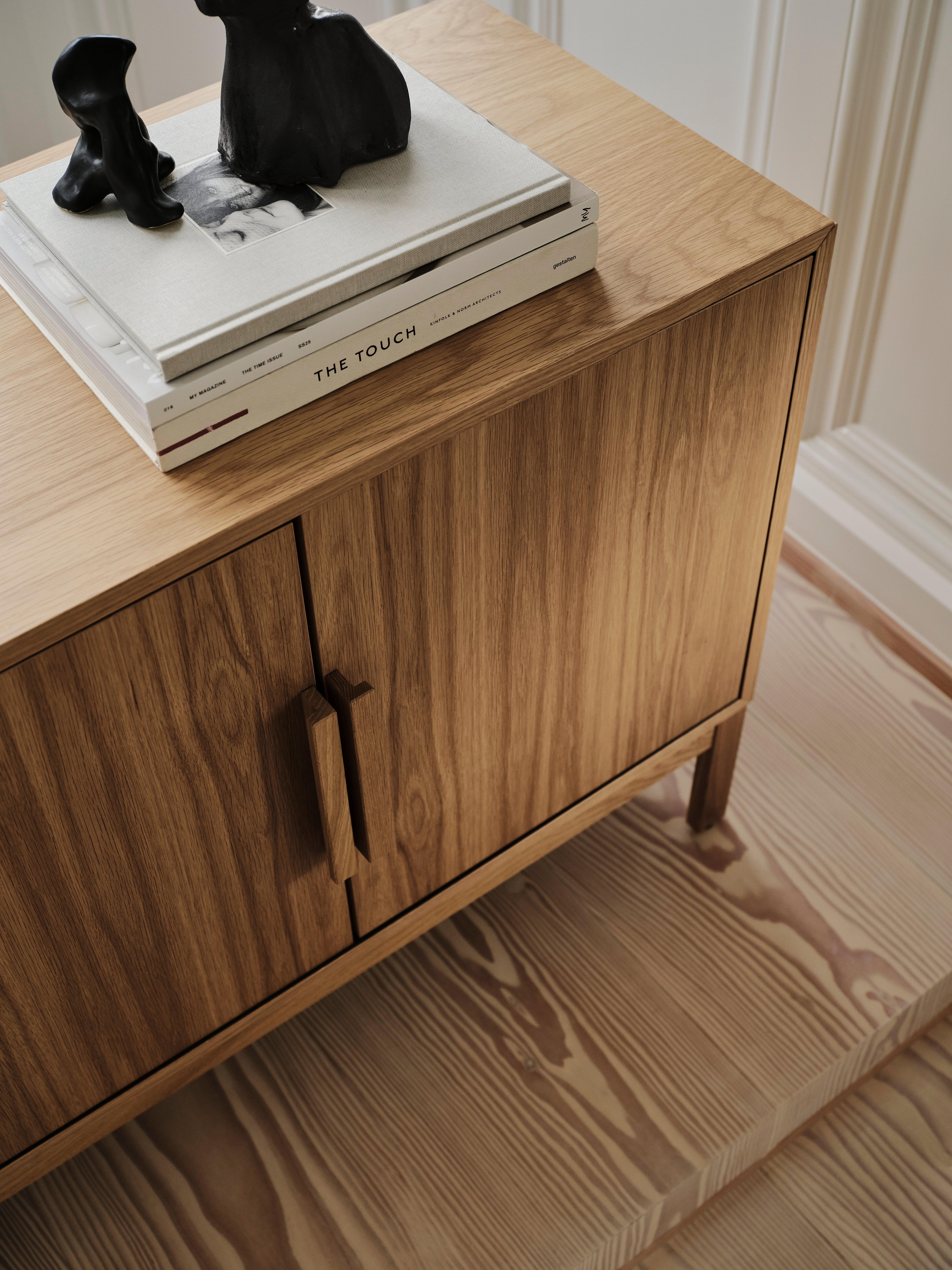 Wooden cabinet with books and black sculptures on top.