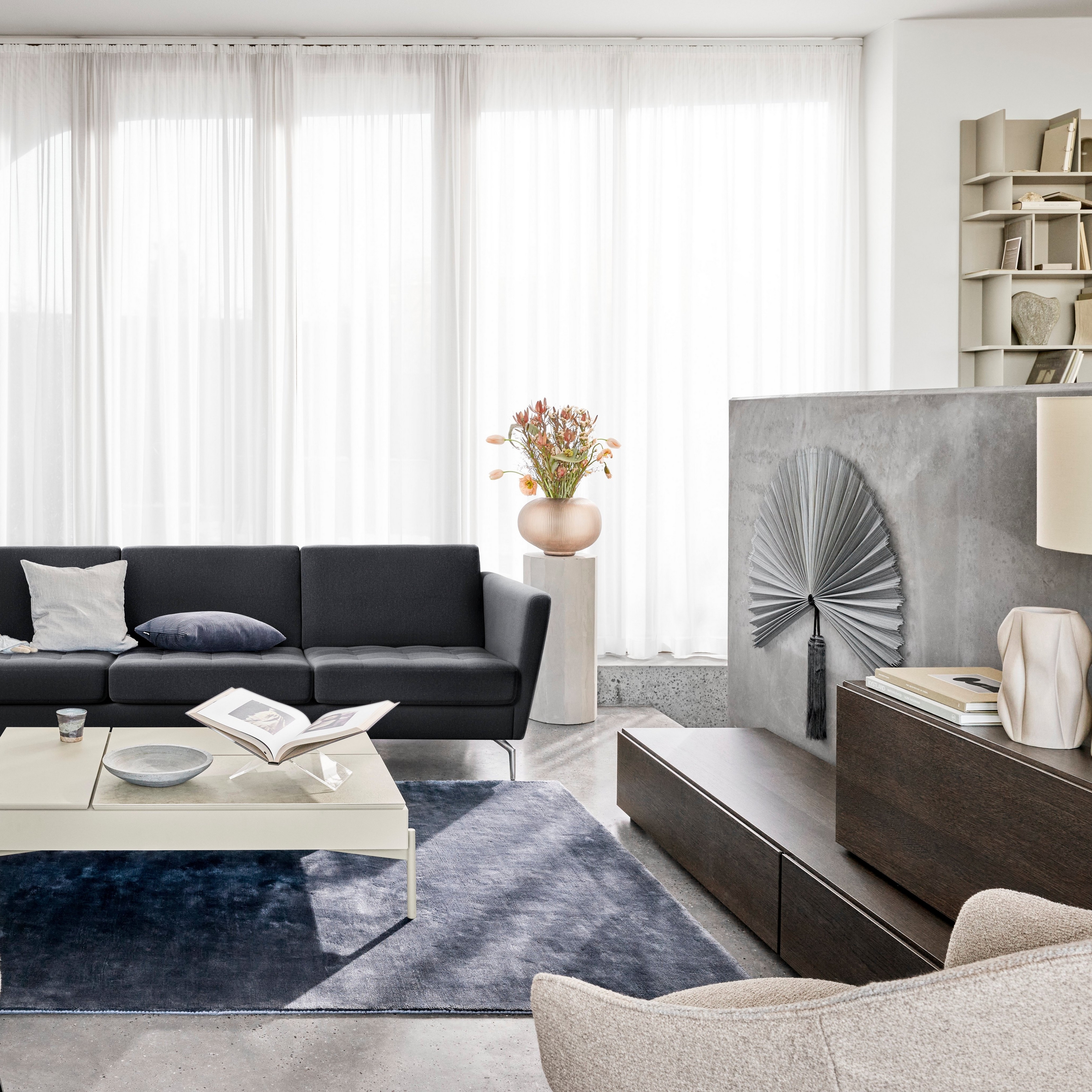 Sala de estar moderna com sofá preto, cadeiras, cortina transparente e elementos decorativos.