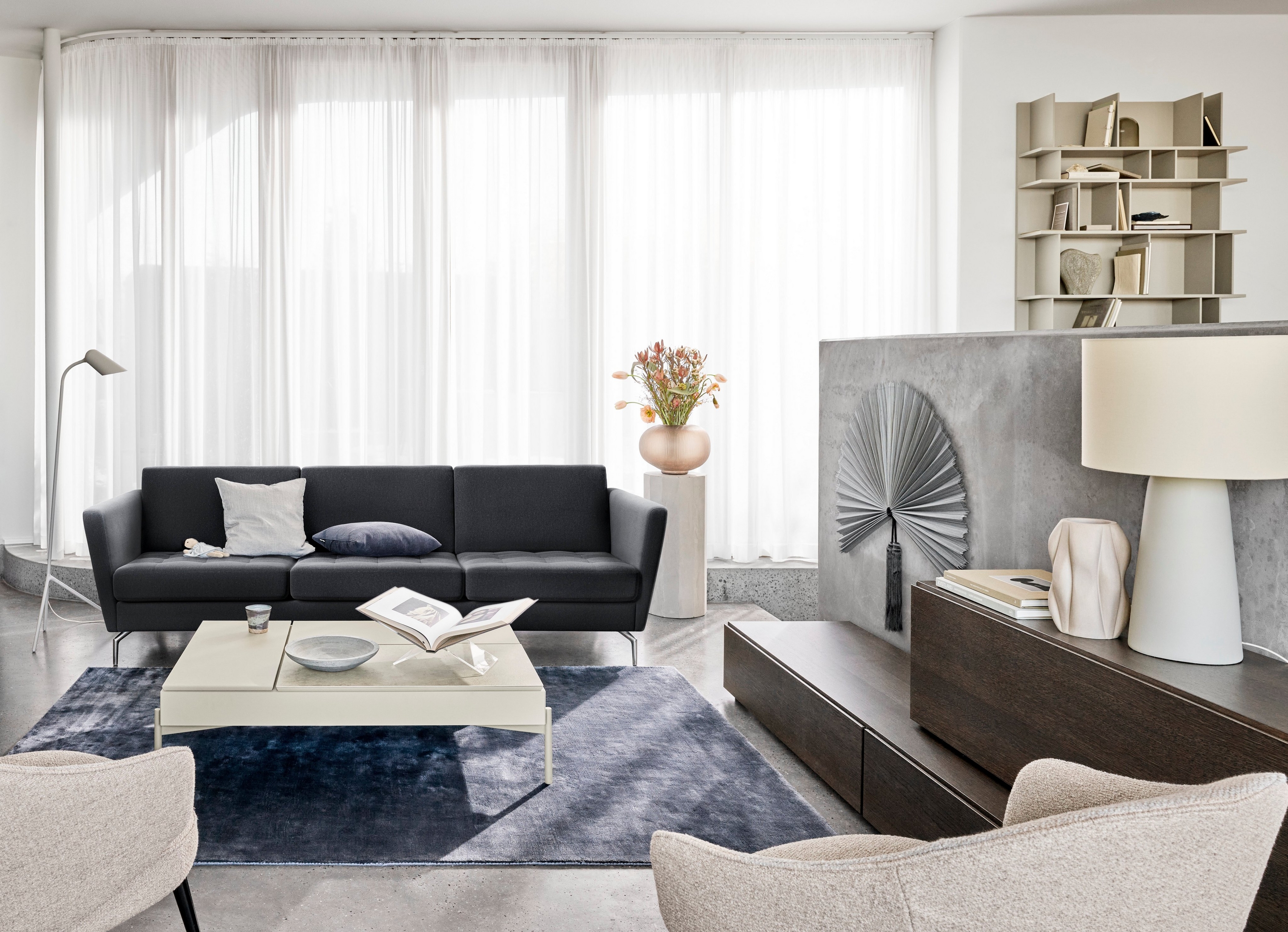 Un salon moderne avec un canapé noir, des chaises, des rideaux transparents et des éléments décoratifs.