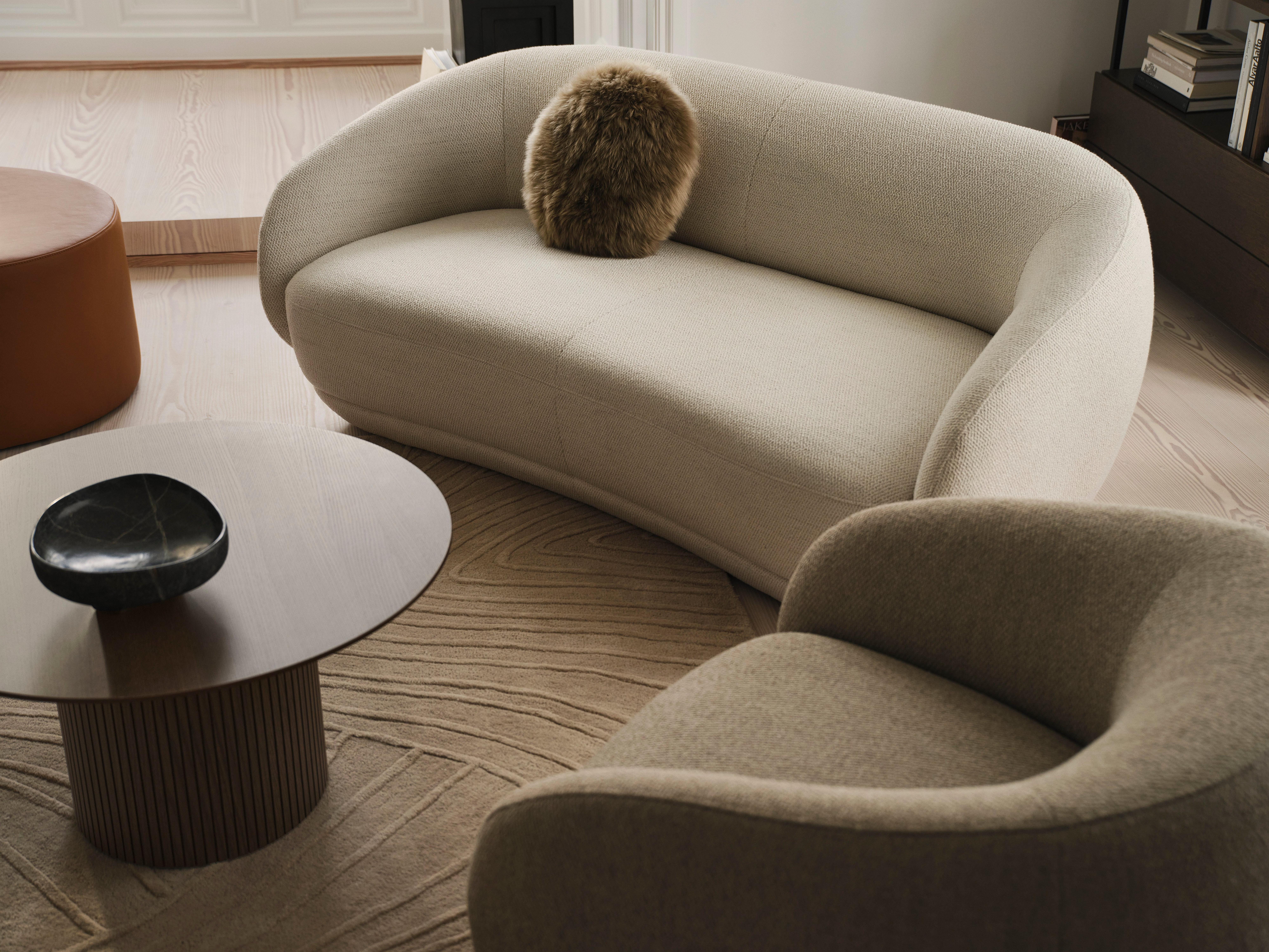 Beige sofa med brun pude, lænestol, rundt bord med sort skål.