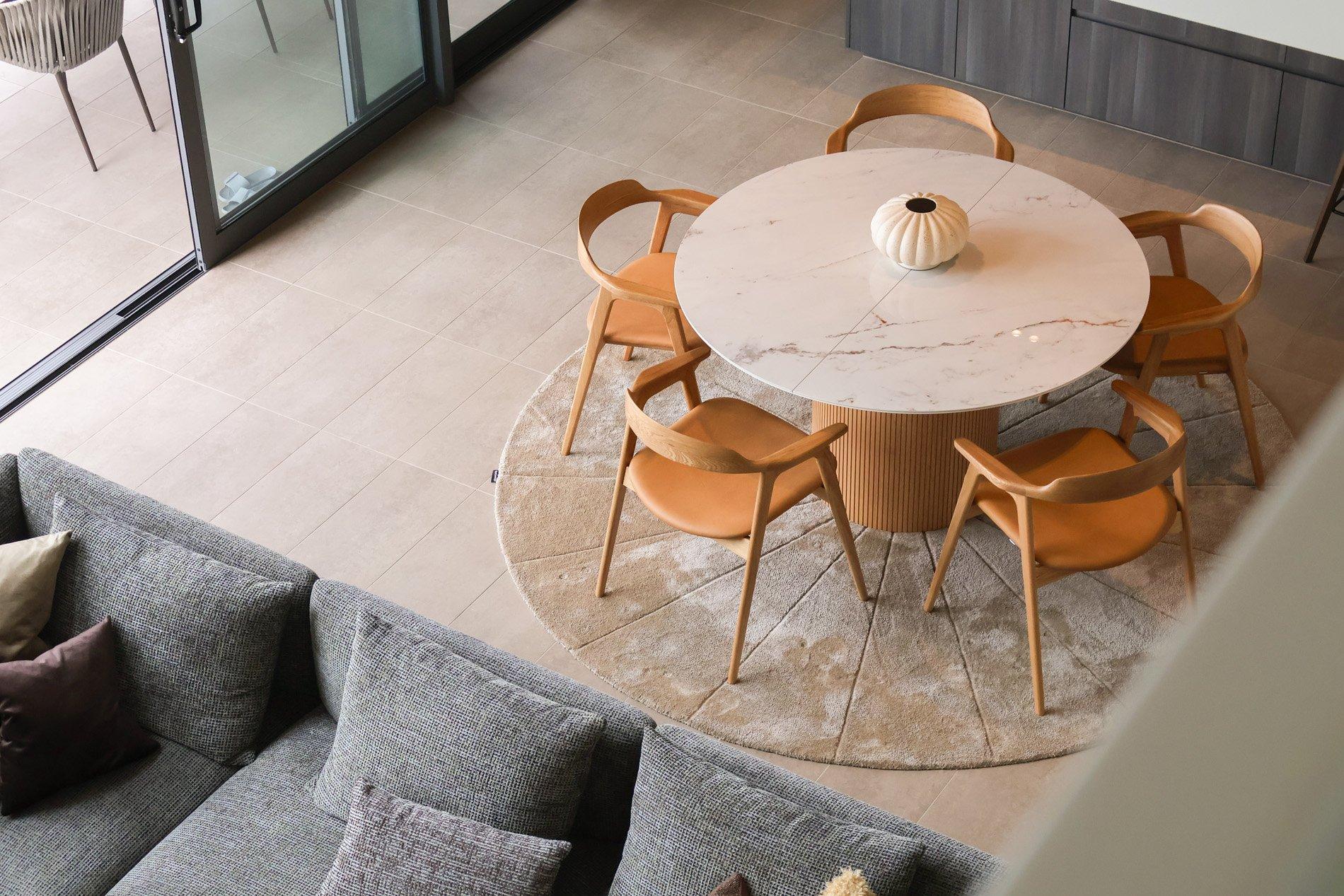 Rundt marmorbord med fem trestoler, sett ovenfra. Grå sofa med puter ved siden av.