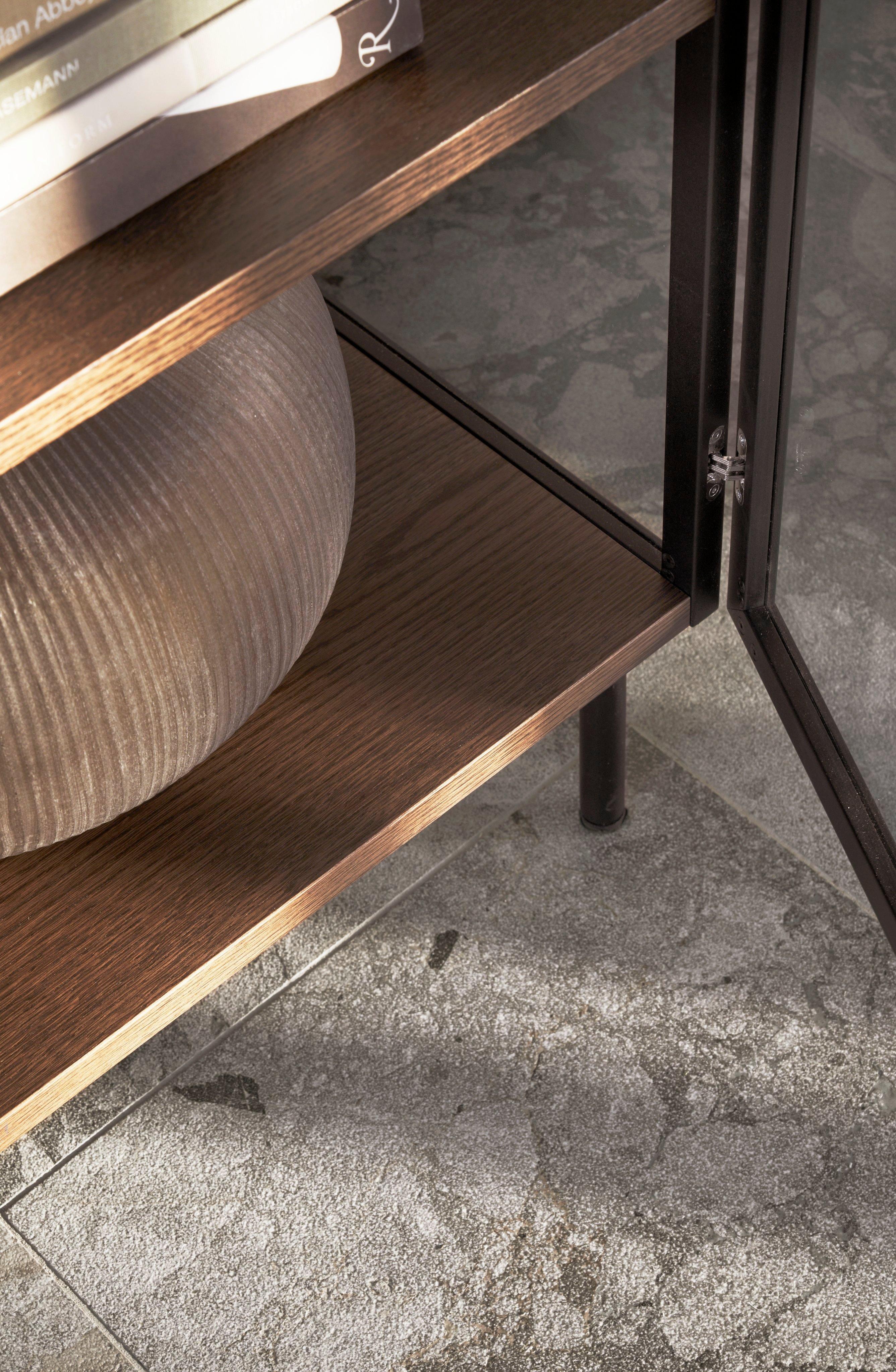 Close-up van een donkere houten plank met een vaas met textuur en boeken, tegen een betonnen vloer.
