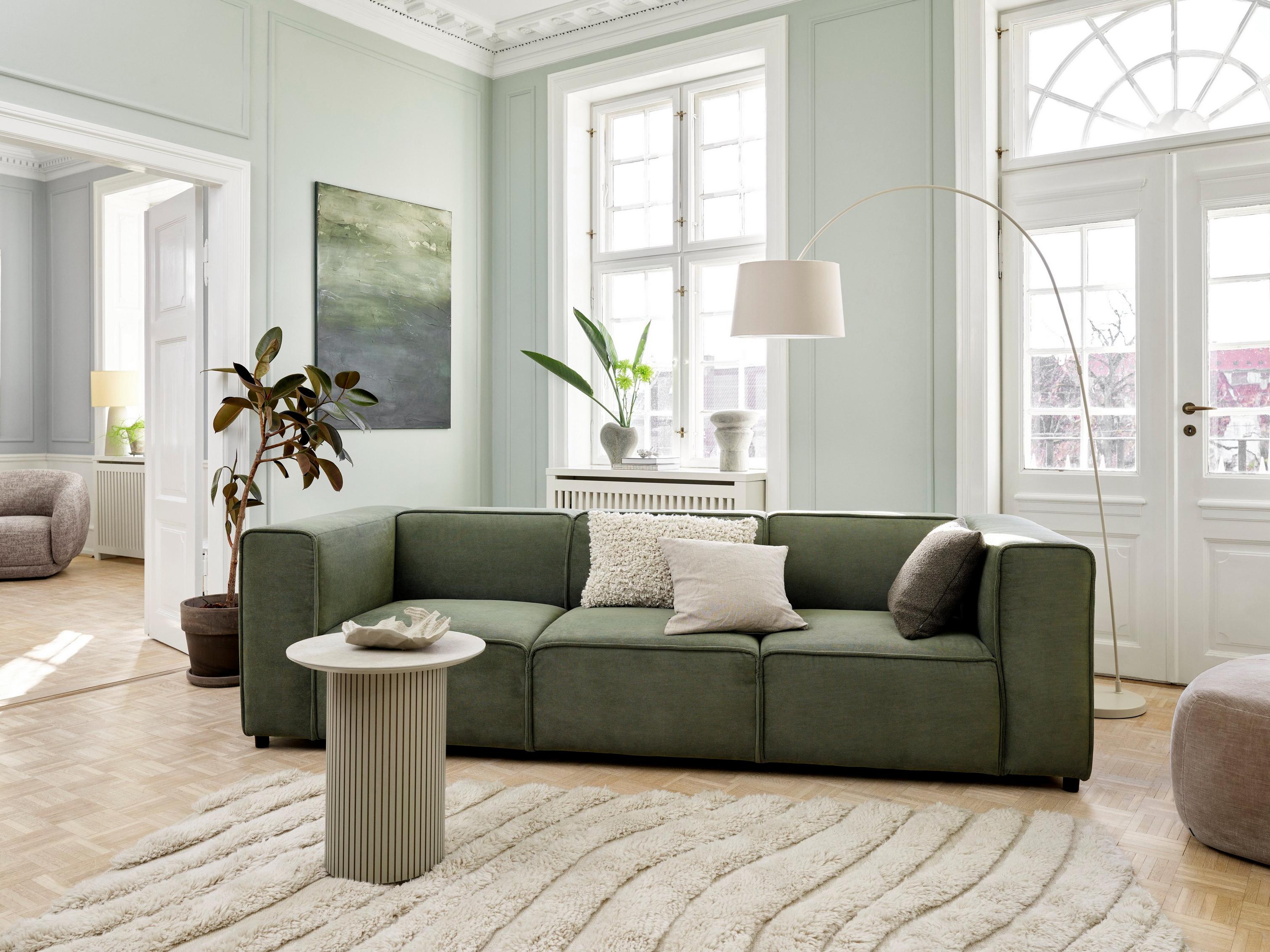 Obývací pokoj ve stylu Japandi s pohovkou Carmo z látky Skagen v zelené barvě.