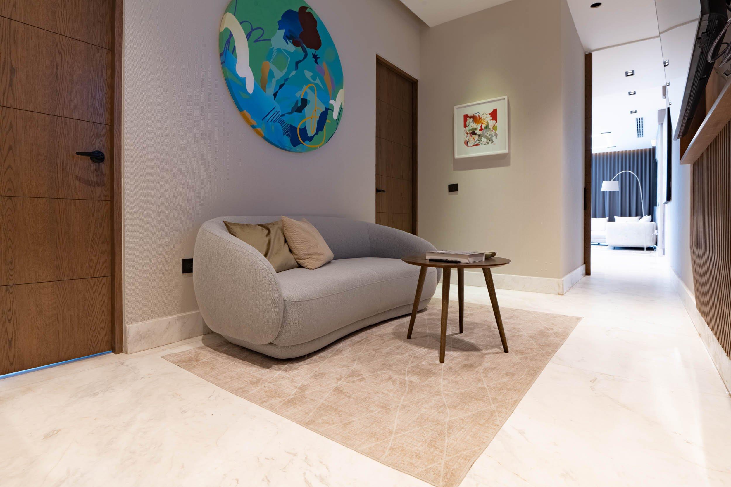 Canapé gris avec coussins et table basse ronde sur tapis beige, dans un couloir moderne.