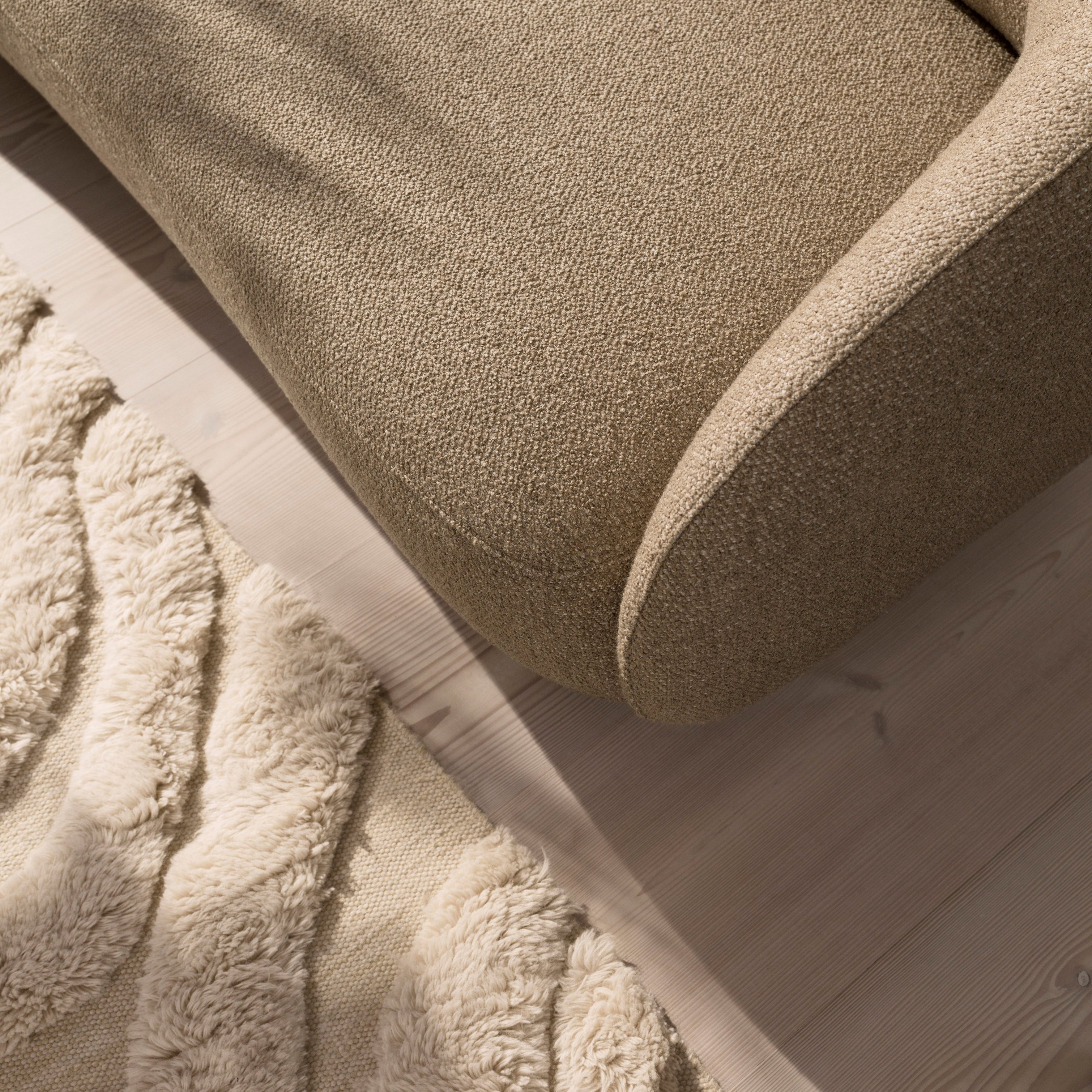 Grande plano do sofá Bolzano em tecido Lazio castanho e do tapete Form em bege.