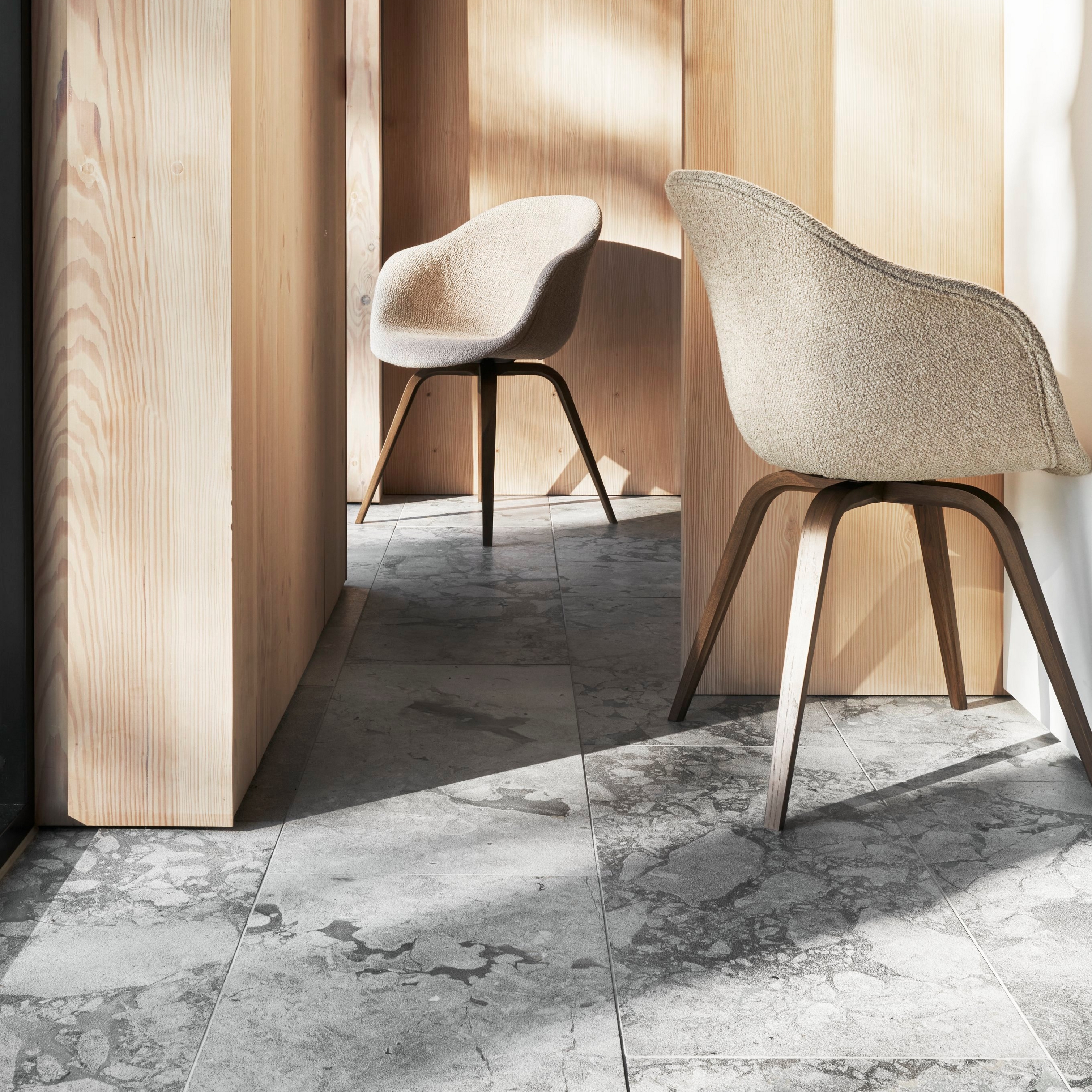 Aurinkoinen sisustus, jossa on kaksi Hauge-tuolia, puuseinät ja marmorilattia.