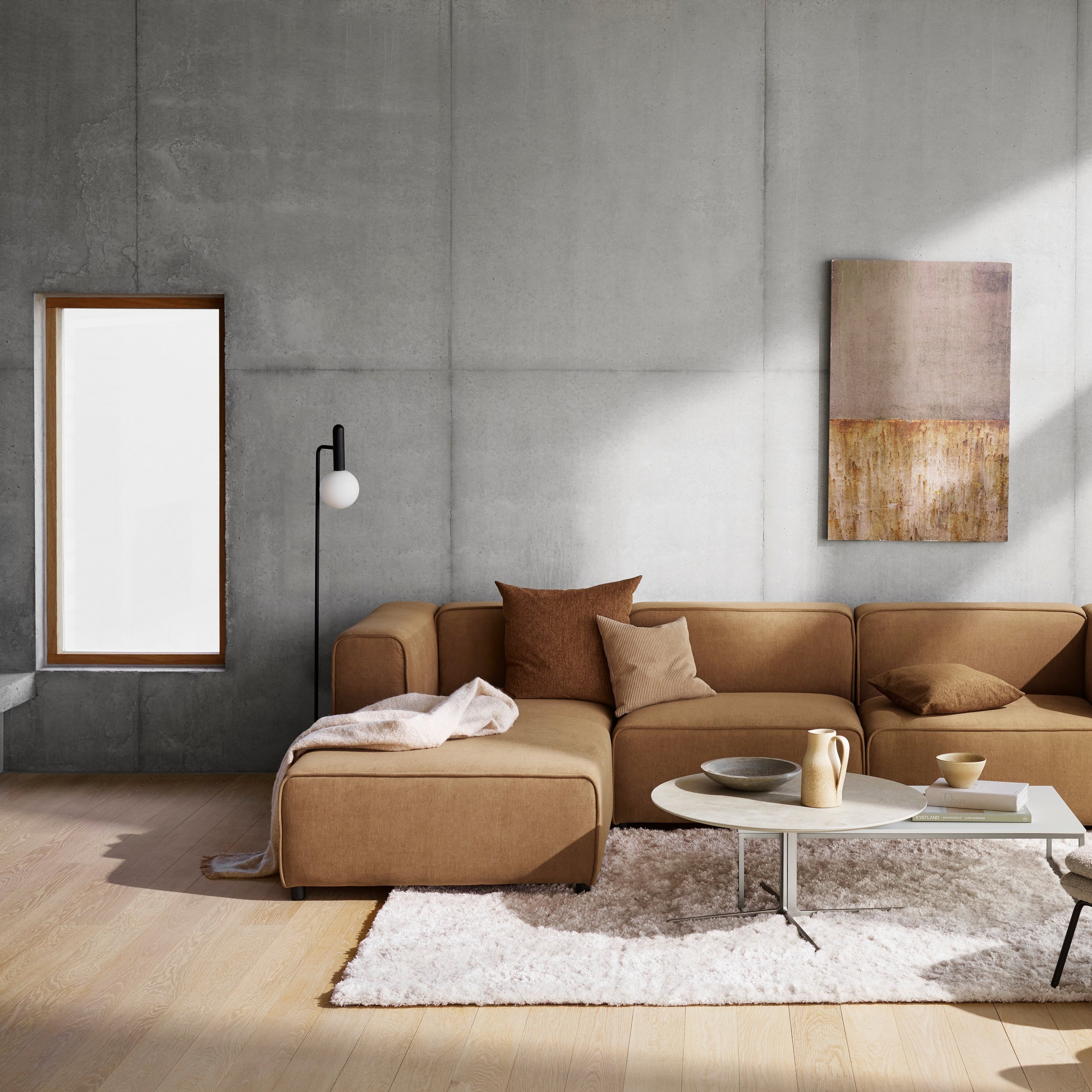 Modernt vardagsrum med beige modulsoffa, abstrakt väggkonst och mjuk matta på trägolv.