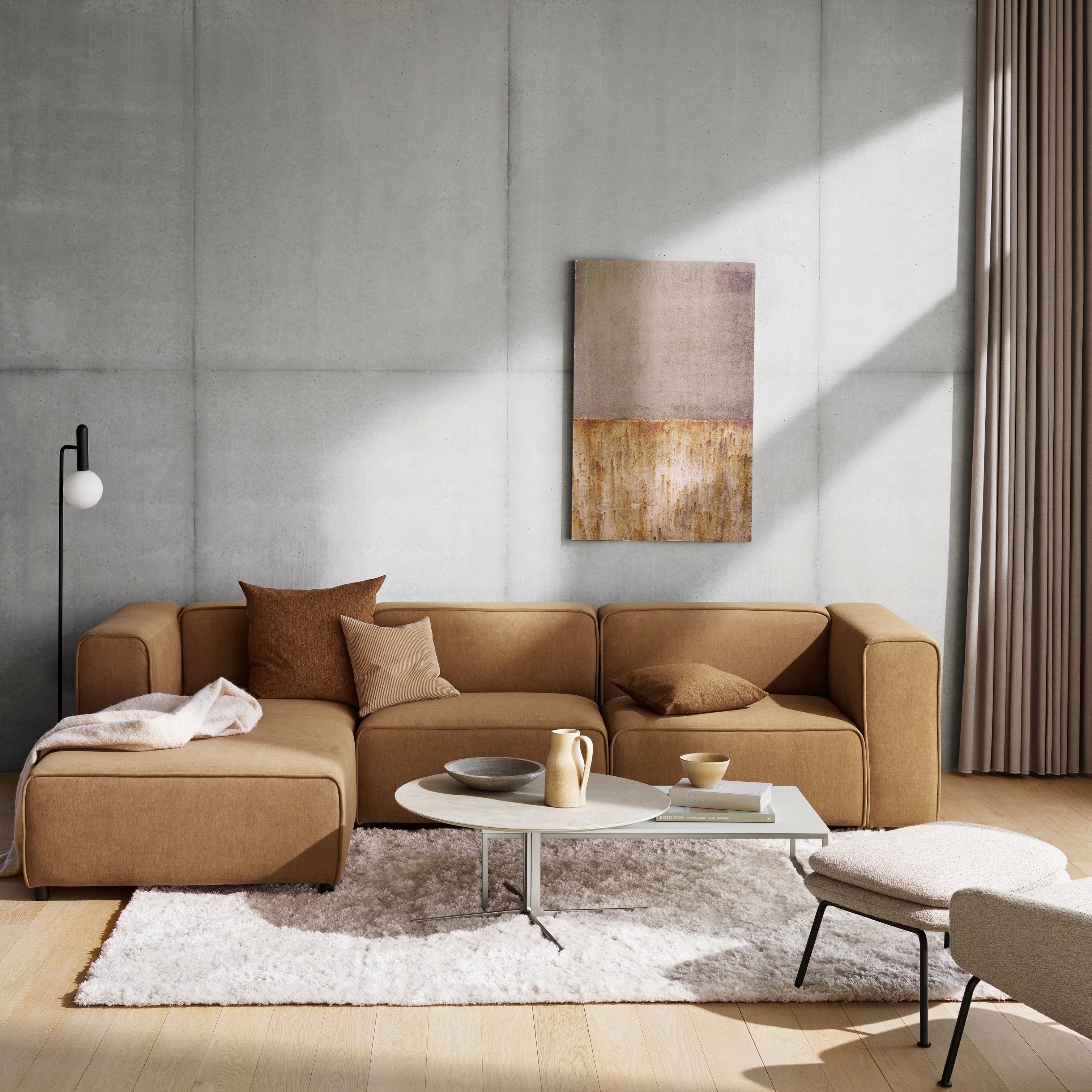 Sala moderna con sofá seccional beige, arte mural abstracto y alfombra peluda sobre suelo de madera.