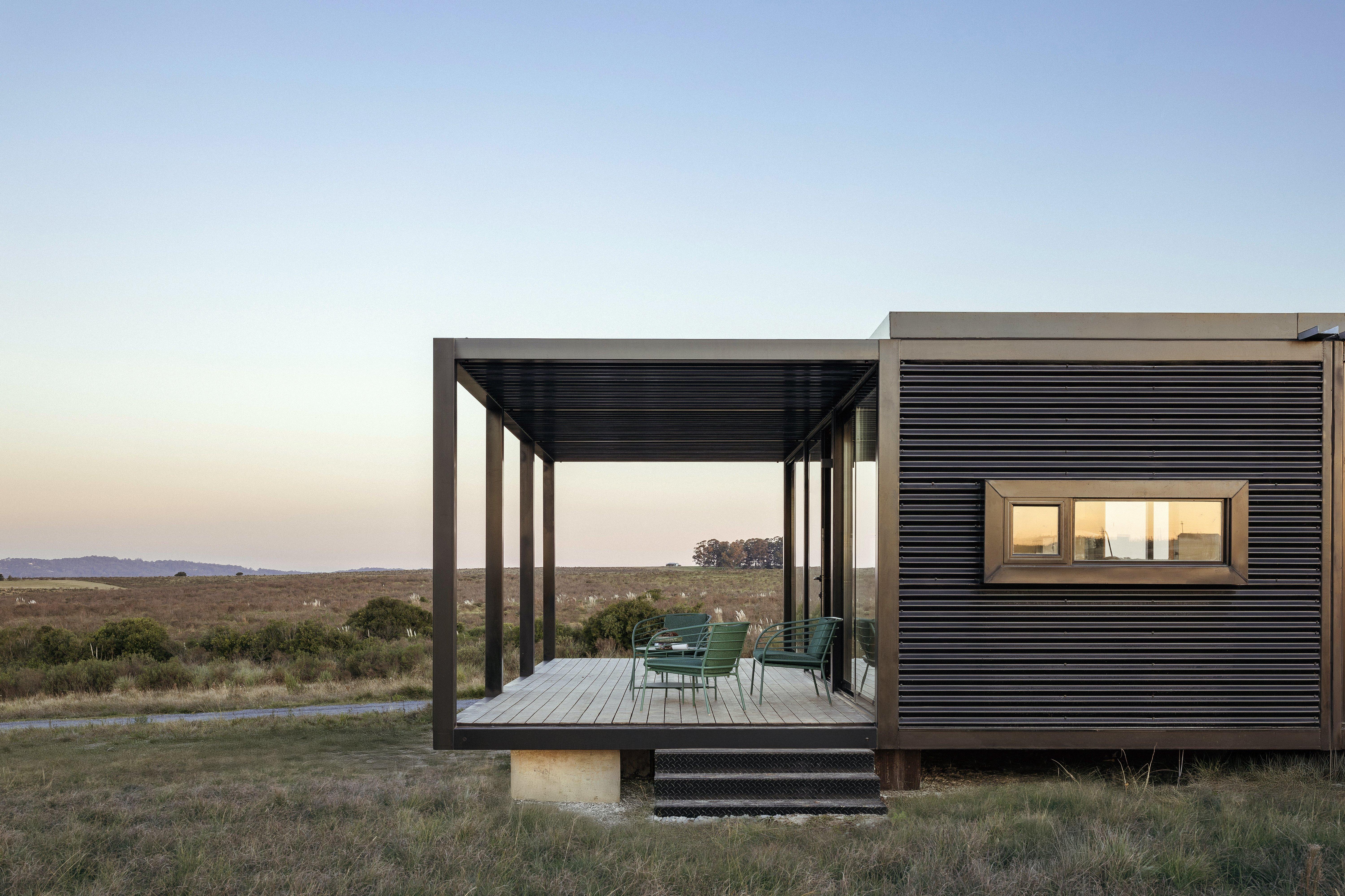 Moderní dům s terasou, zelené židle, výhled na krajinu.