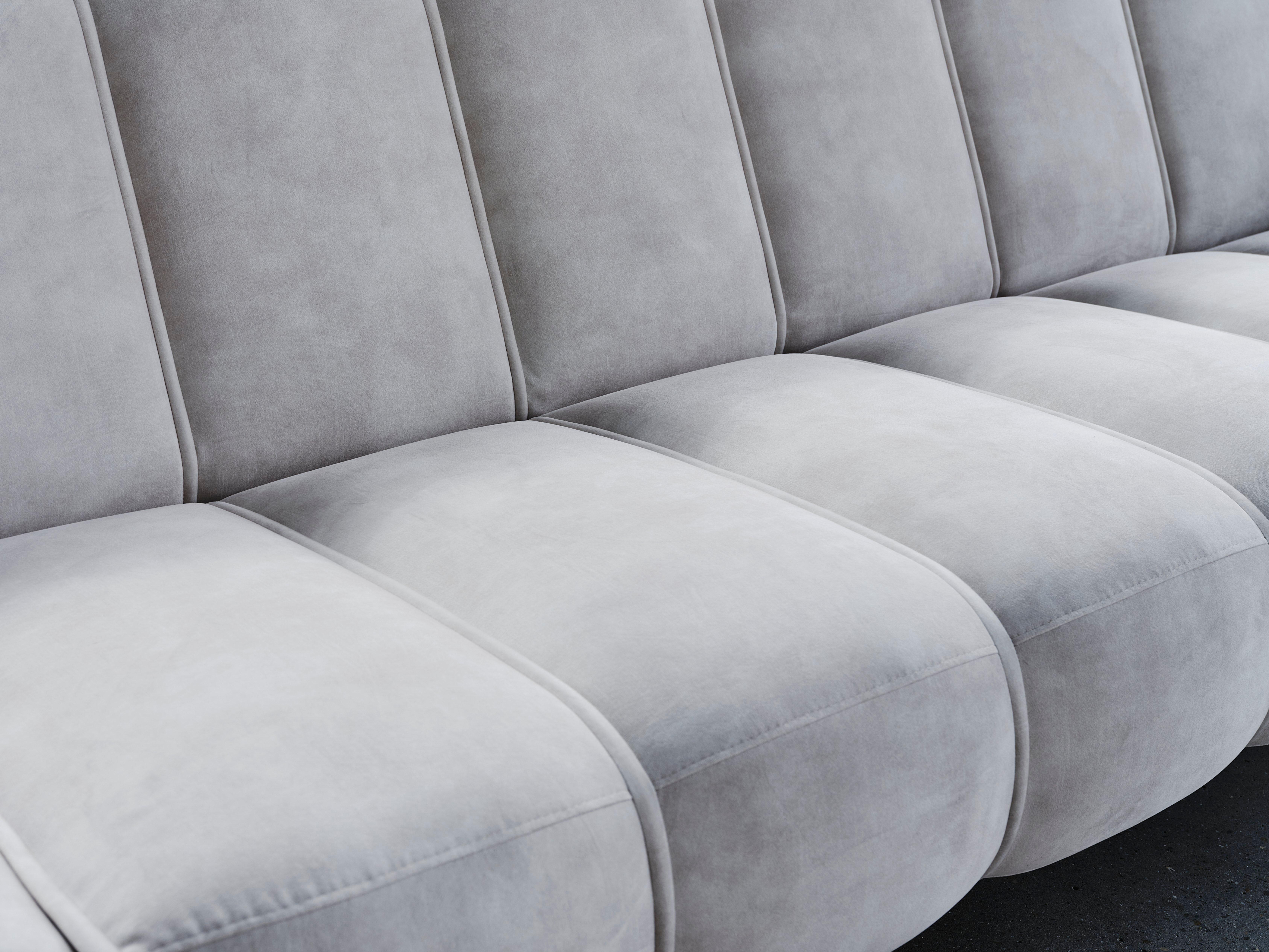 Harmaa sohva, jossa on pehmeät tyynyt ja pystysaumat.