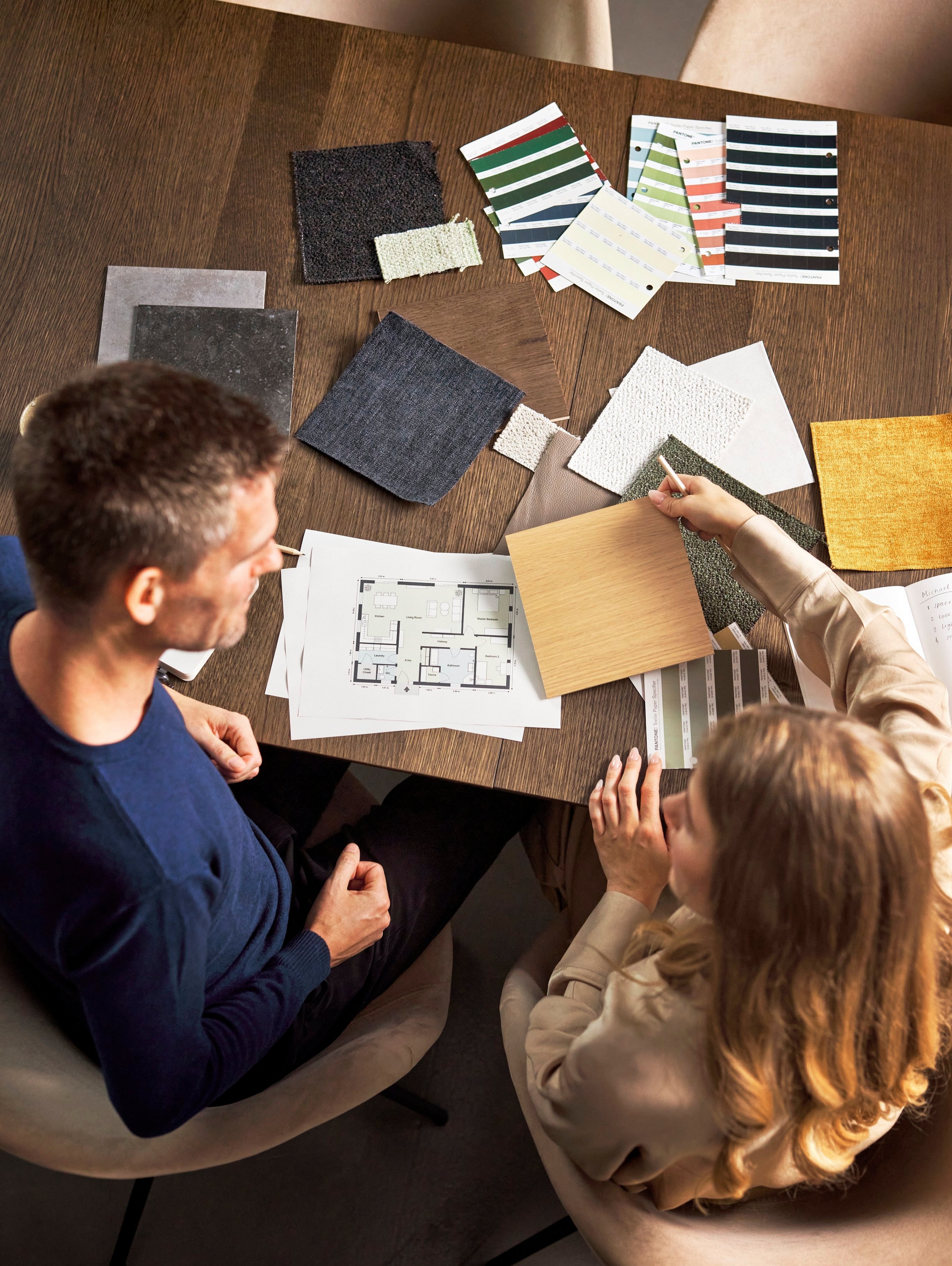 Overhead view of two people discussing material samples and floor plans at a table.