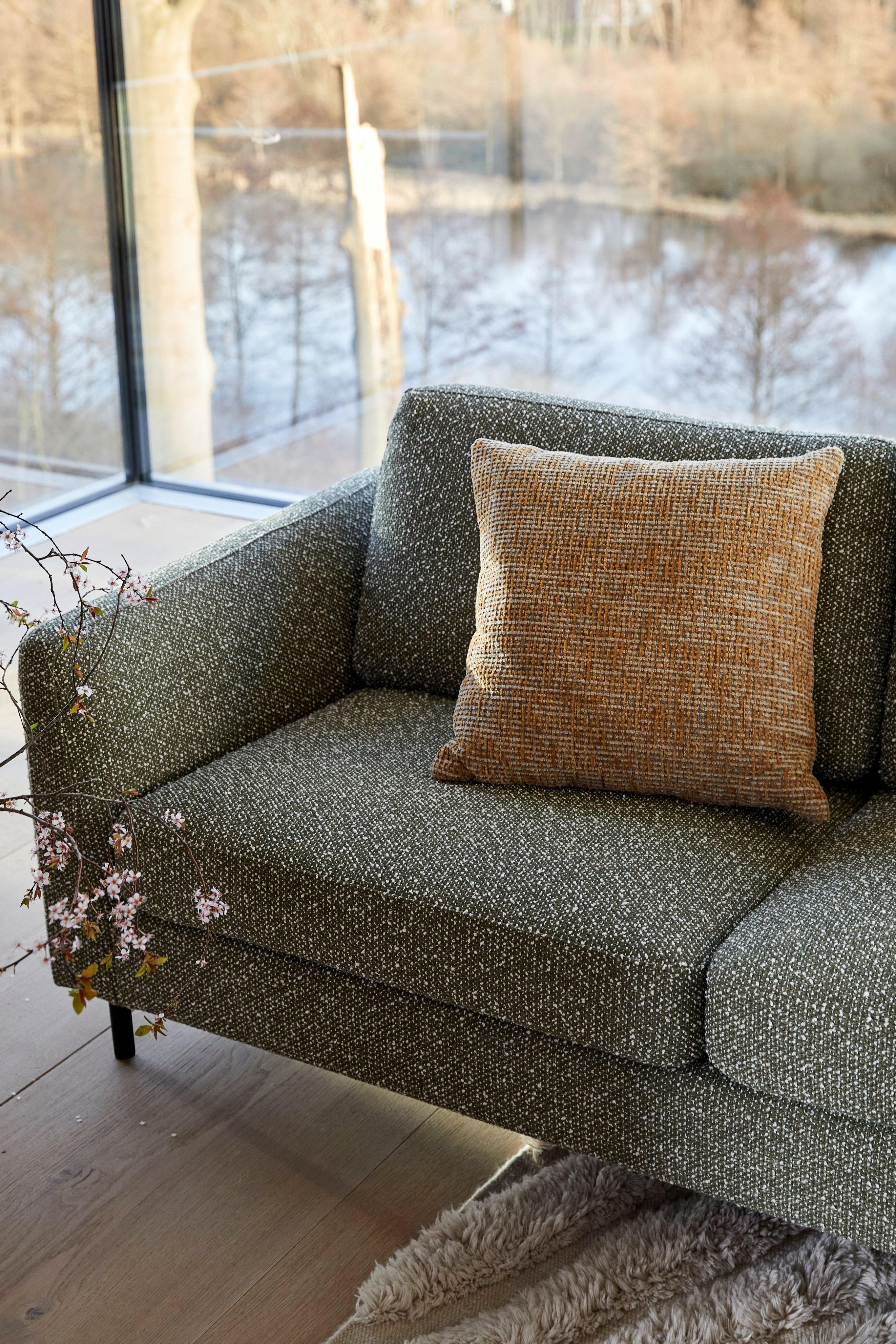 Lifestyle image of BoConcept Indivi corner sofa in green Avellino fabric, showing the 'Form' rug in cream/white, 'Salamanca' cushion in mustard Tuscany fabric