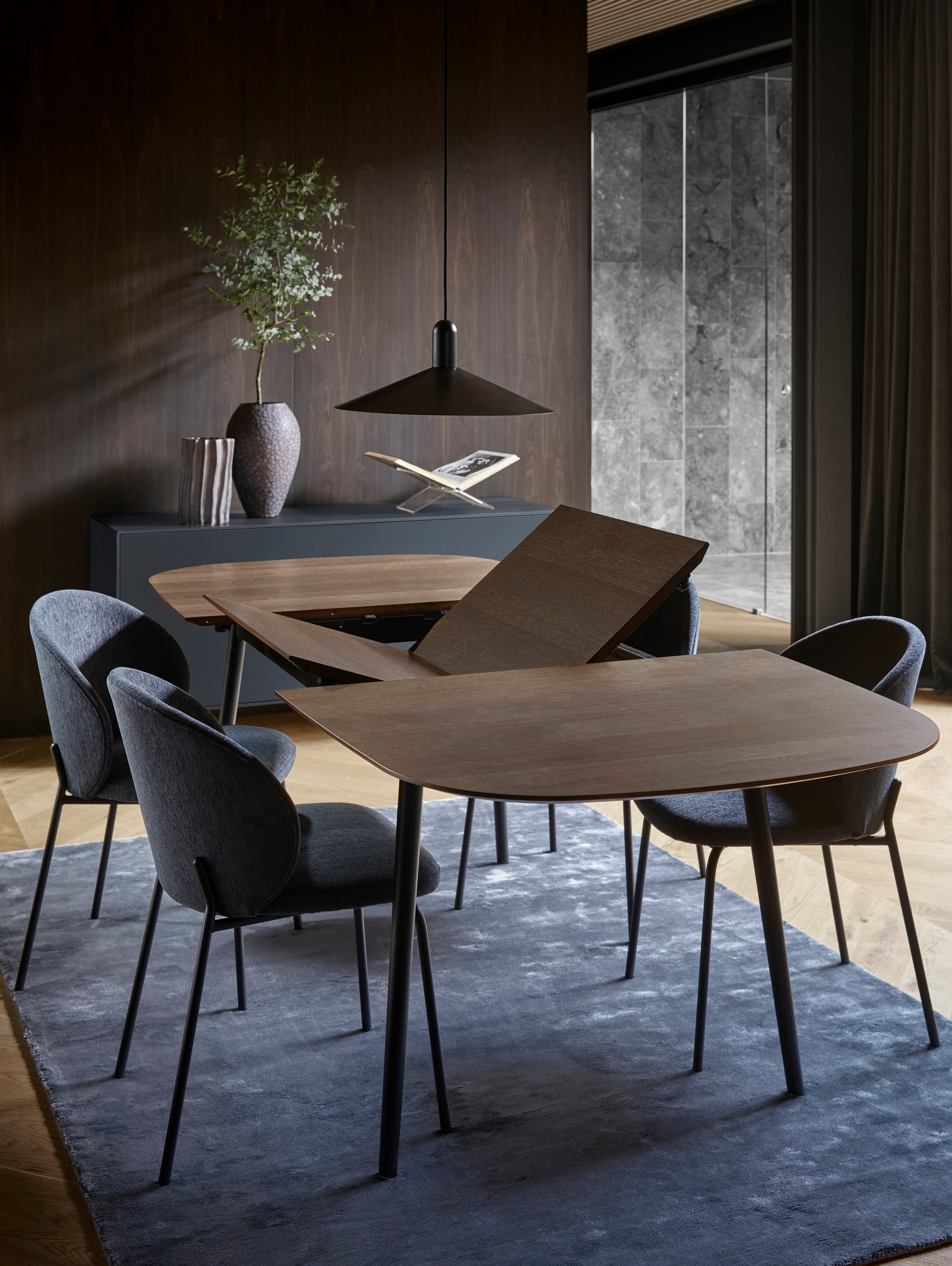 Contemporary dining room with extendable table, dark chairs, pendant light and vase with greenery