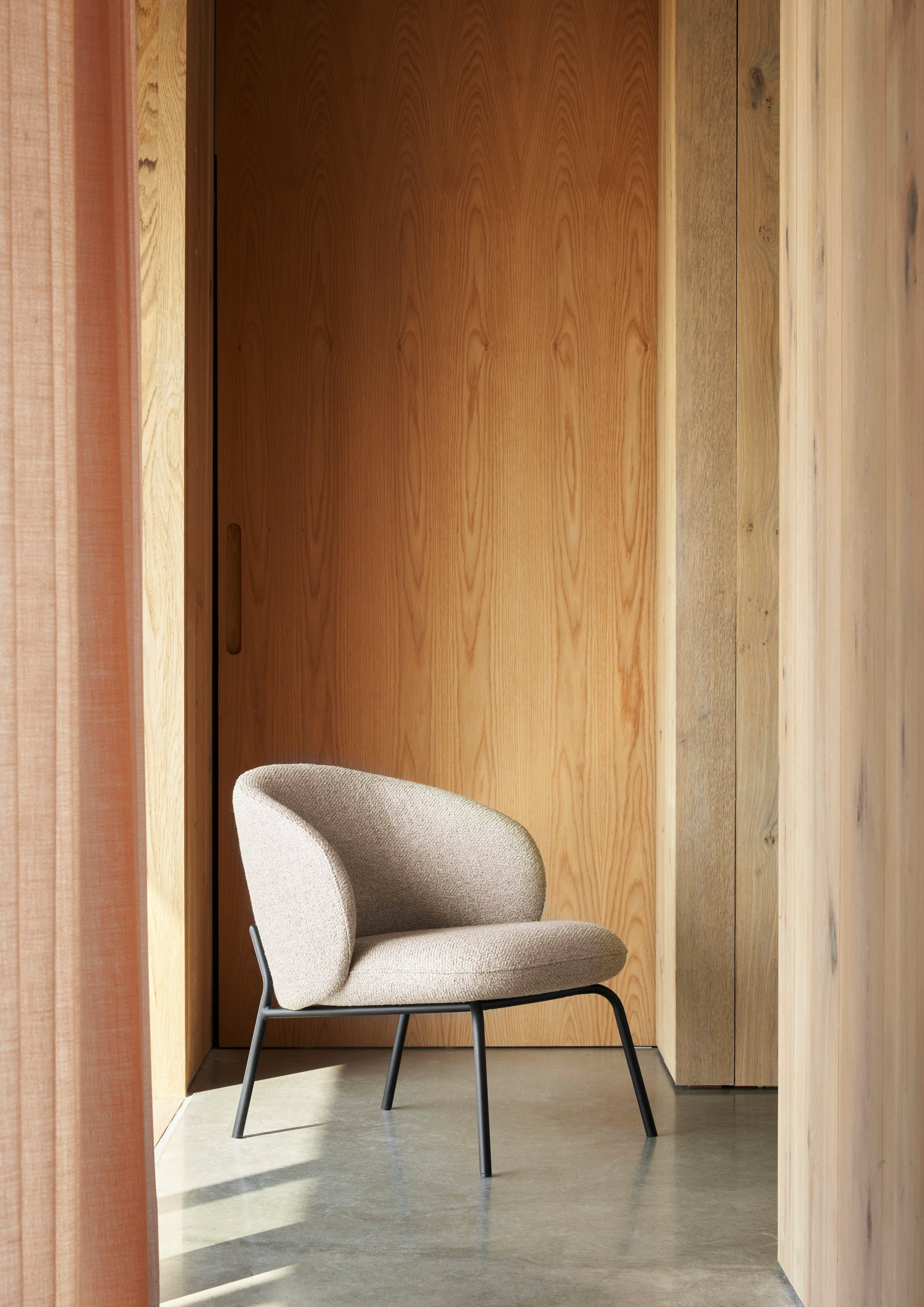 Modern chair with beige upholstery and black frame in a sunlit wooden interior.
