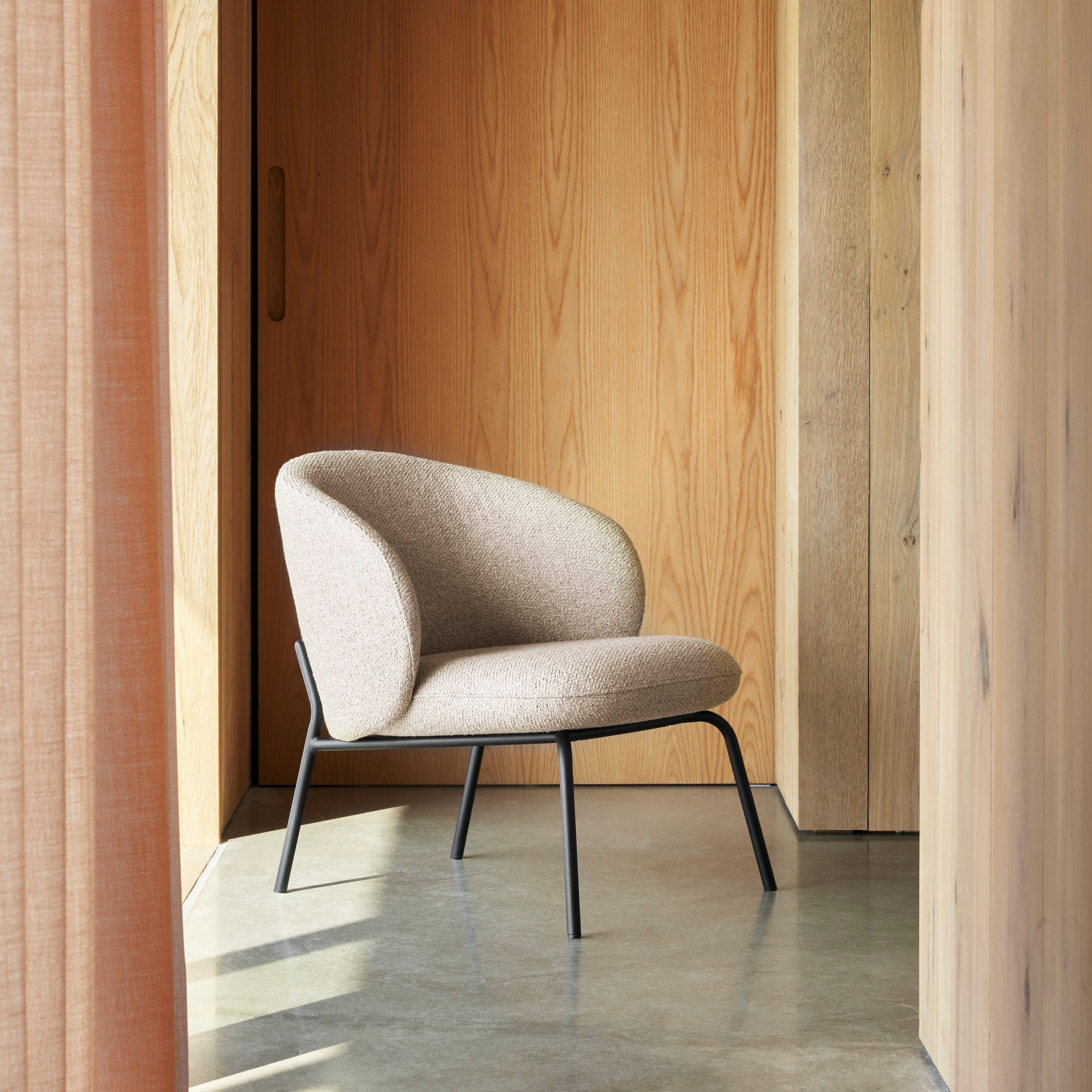 Moderne stol med polster i beige samt sort ramme opstillet i solbelyst indretning med træ.