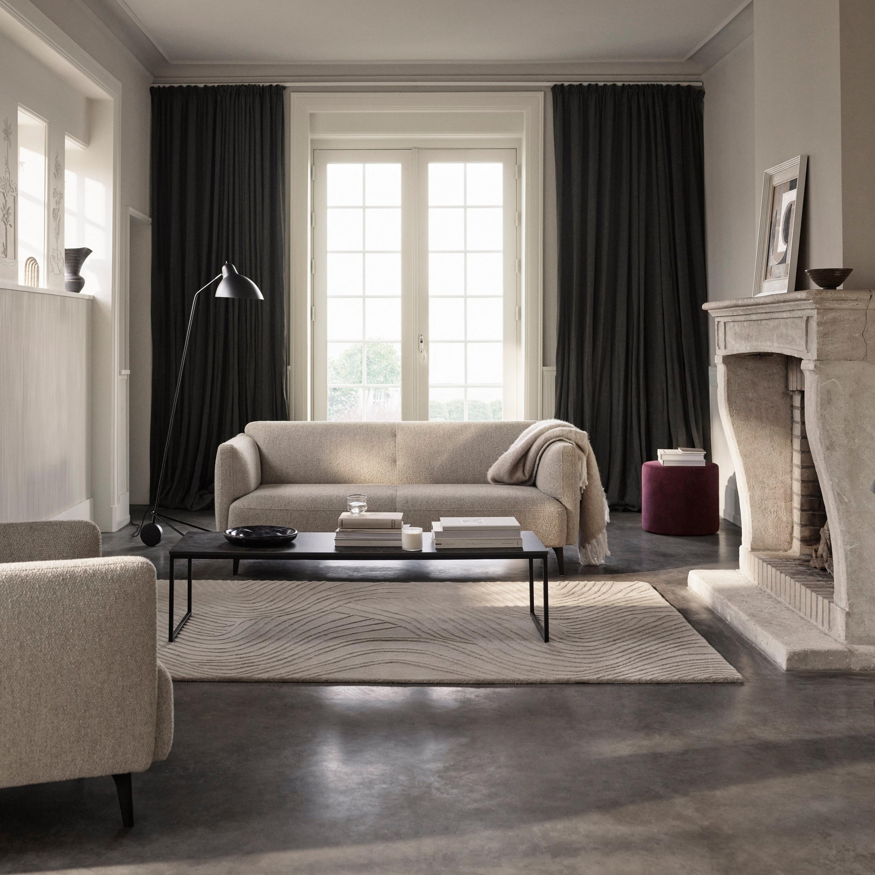 Elegant living room with neutral sofas, a black coffee table, and a stone fireplace, framed by dark curtains and French doors.