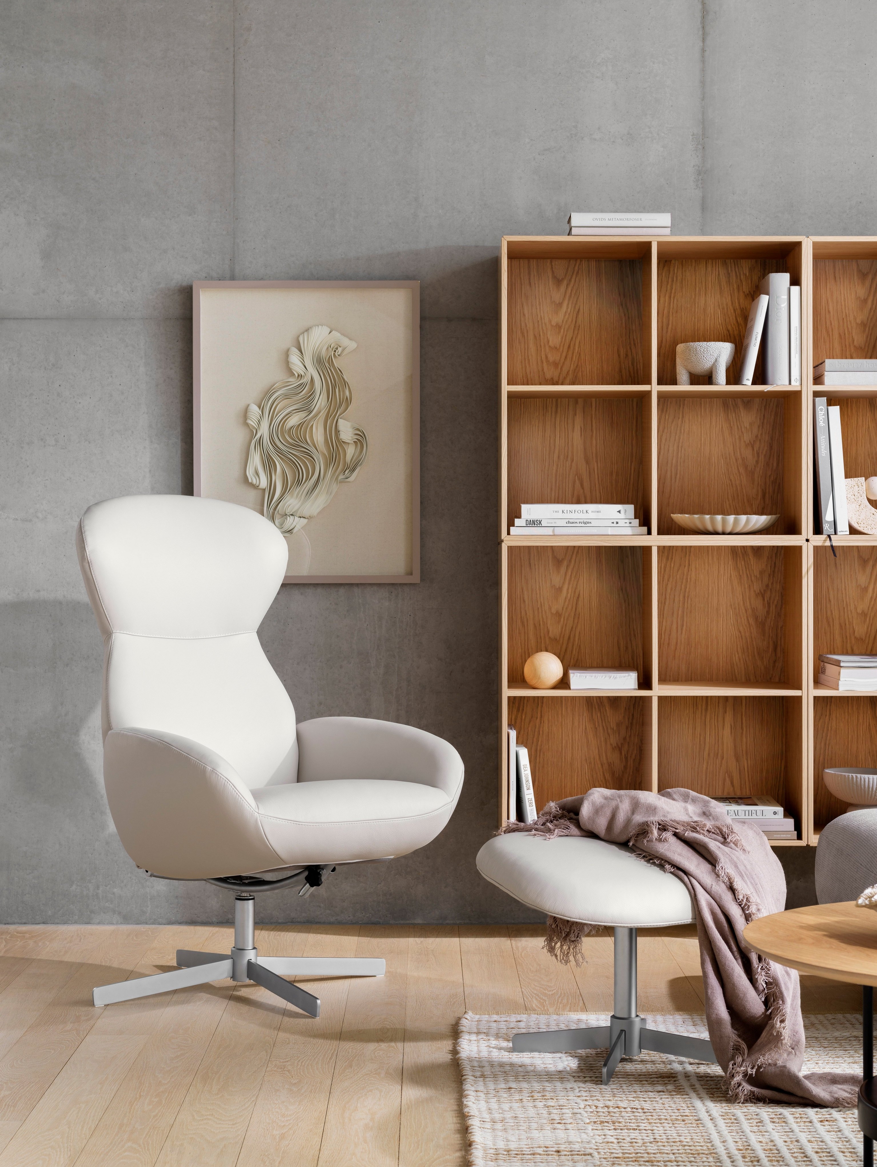 Biały fotel rozkładany Athena z podnóżkiem i drewnianą półką na książki Como w przytulnym pomieszczeniu.
