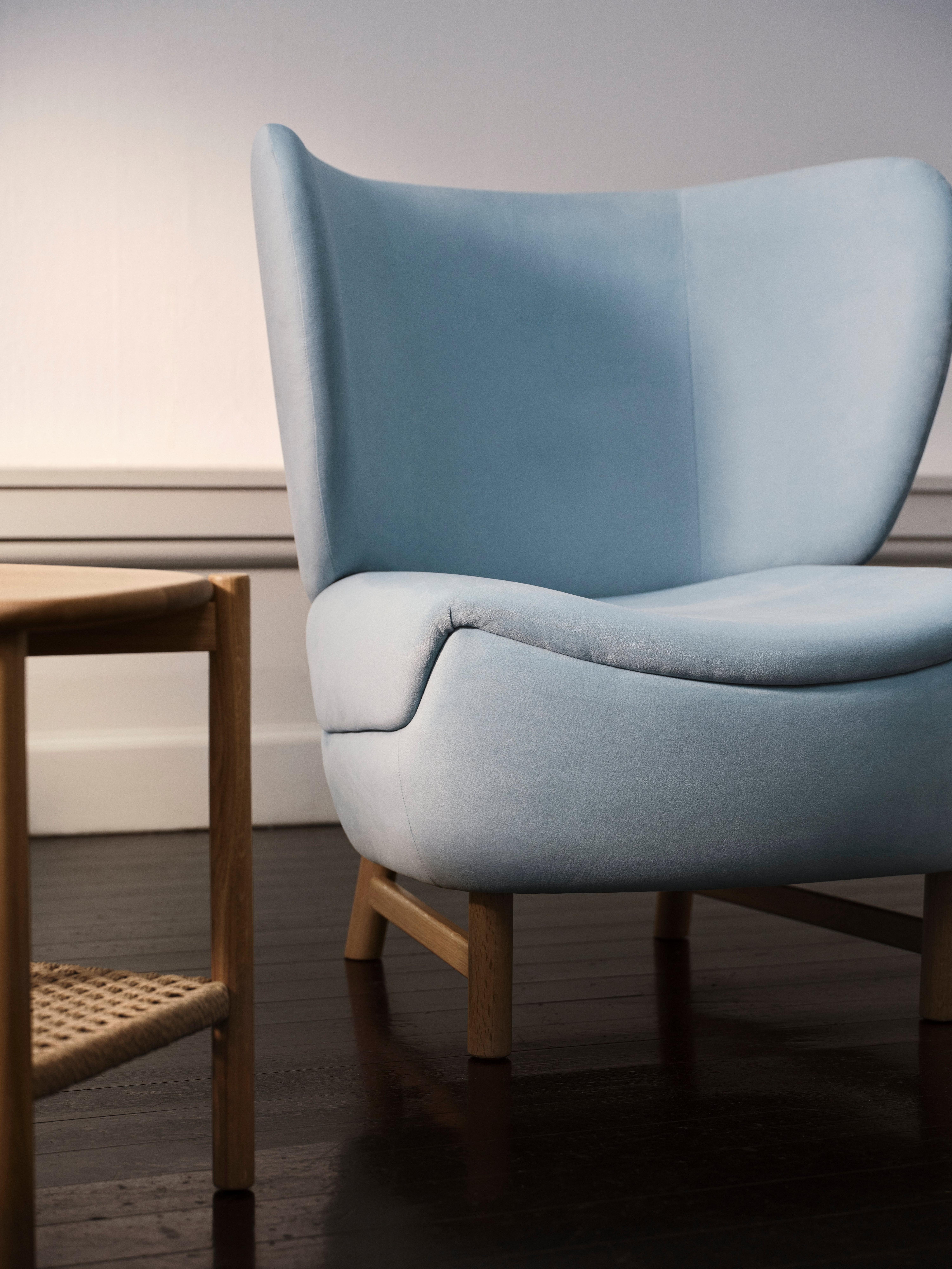 Lys blå stol med treben ved siden av et lite bord med flettet hylle.